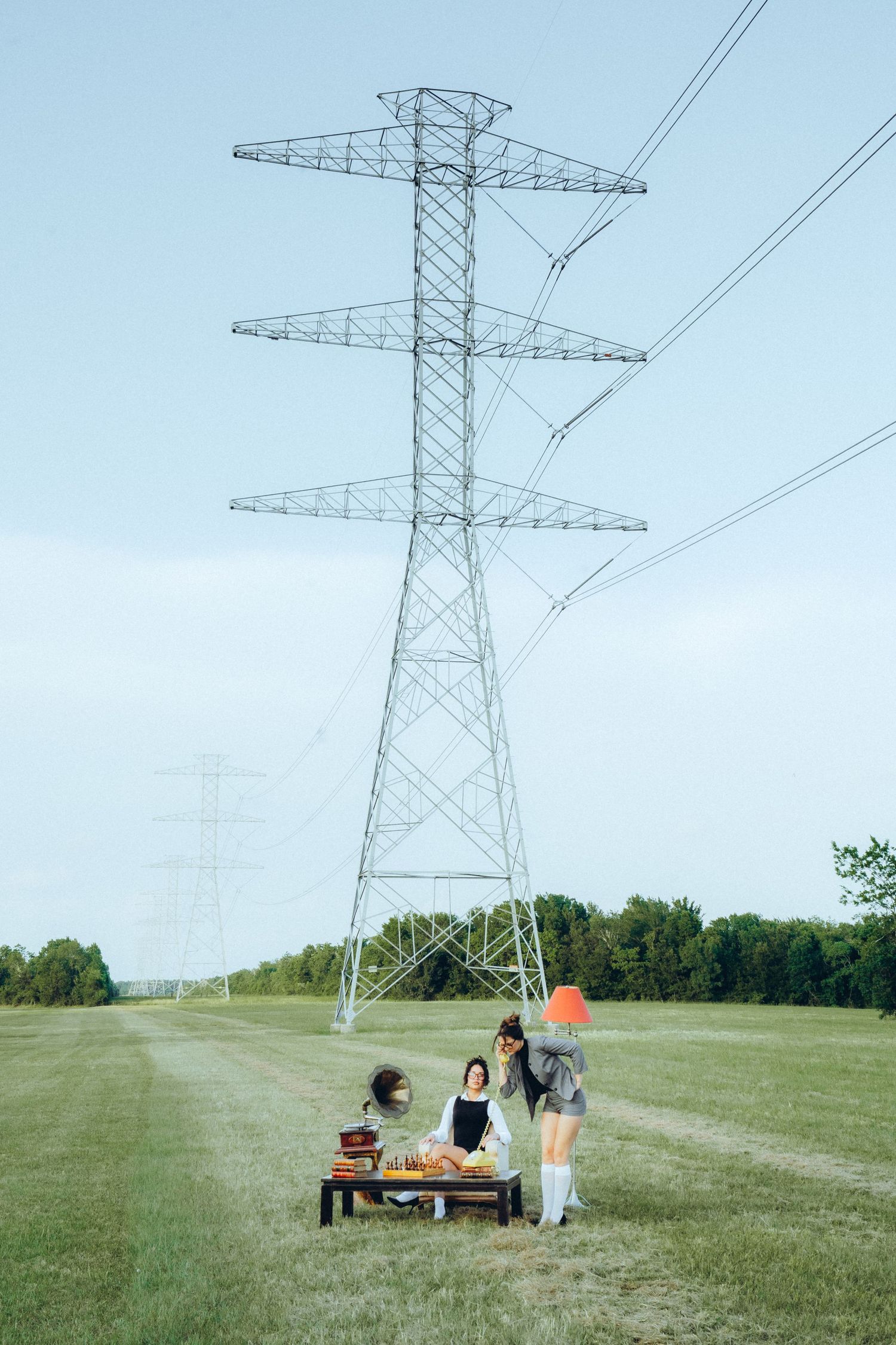 Group having a picnic at a wooden table under large electrical transmission tower in grassy field on sunny day.
