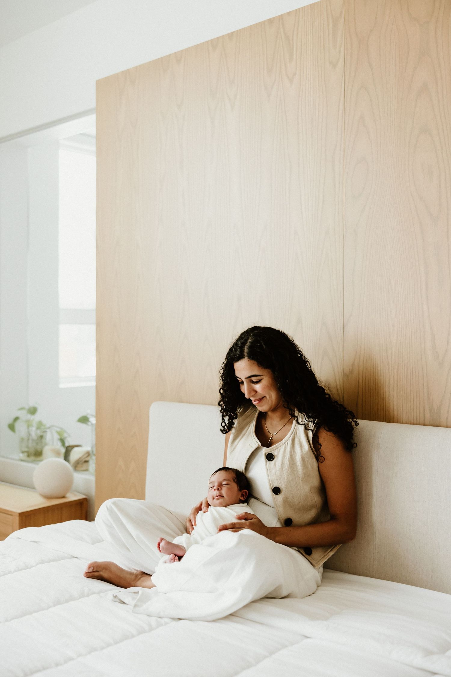 A tender moment captured in a bright bedroom with white bedding and wood panel walls.