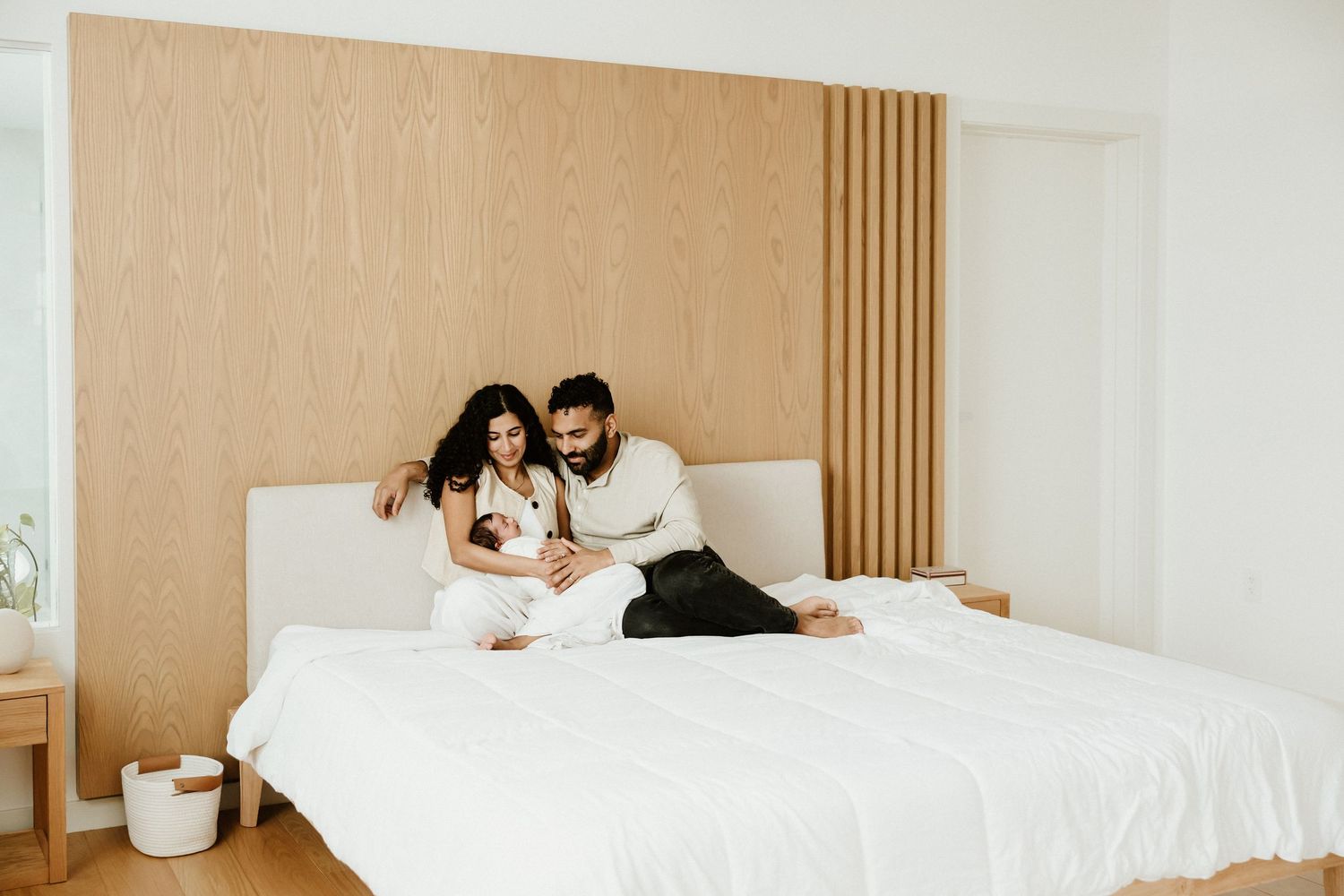 A modern minimalist bedroom interior with wooden slat wall panels and white bedding in natural light.