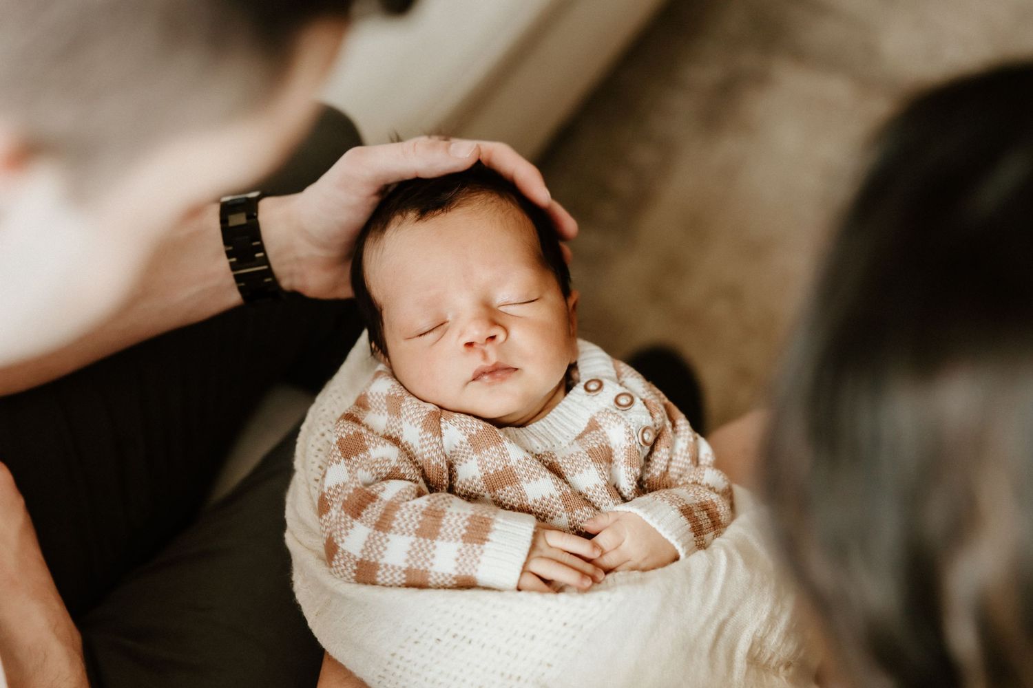 A peacefully sleeping newborn baby wrapped in a cozy brown checkered blanket during a gentle moment.