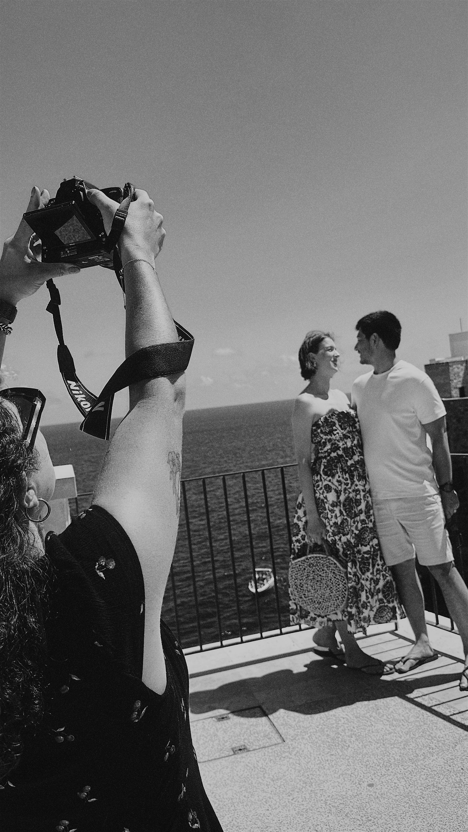 Black and white sequence of people dancing together on a balcony overlooking the ocean.