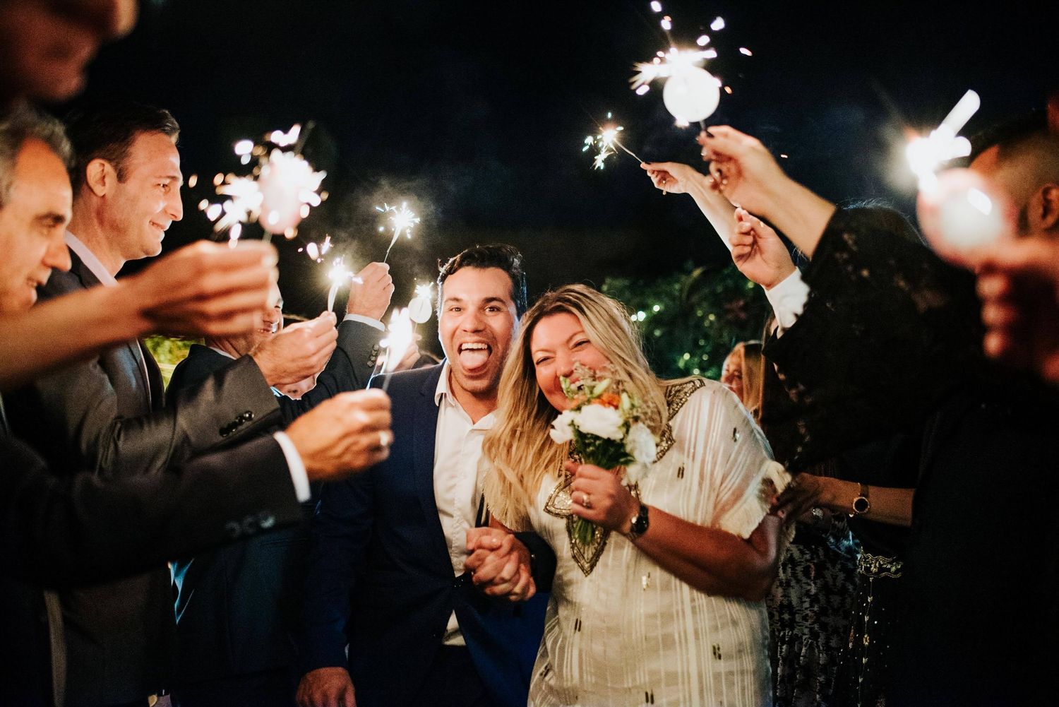Sparklers illuminate the night as wedding guests celebrate outdoors with glowing lights.