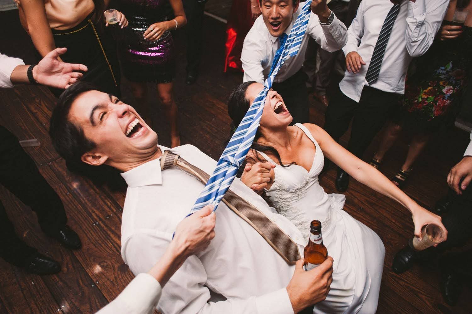 Wedding guests dancing and celebrating energetically on a dark wooden dance floor at a reception party.