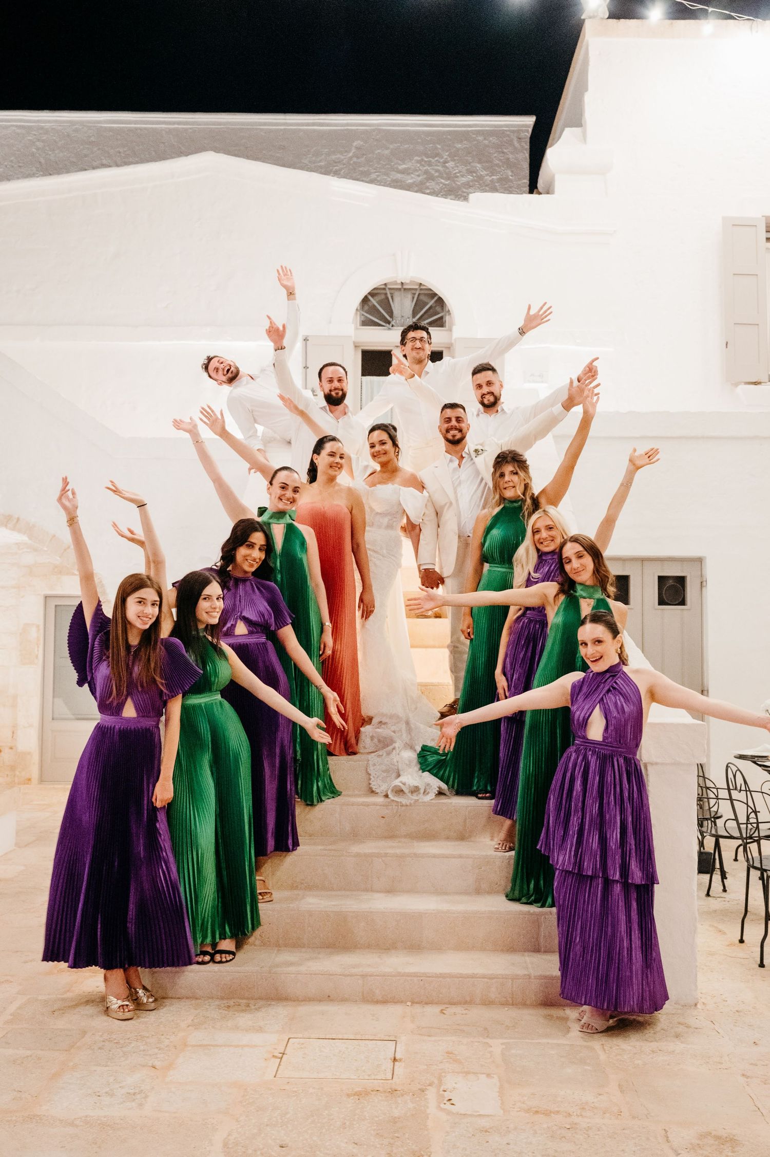 Wedding party in purple and green dresses pose playfully in sequence of coordinated jumping photos in white venue.