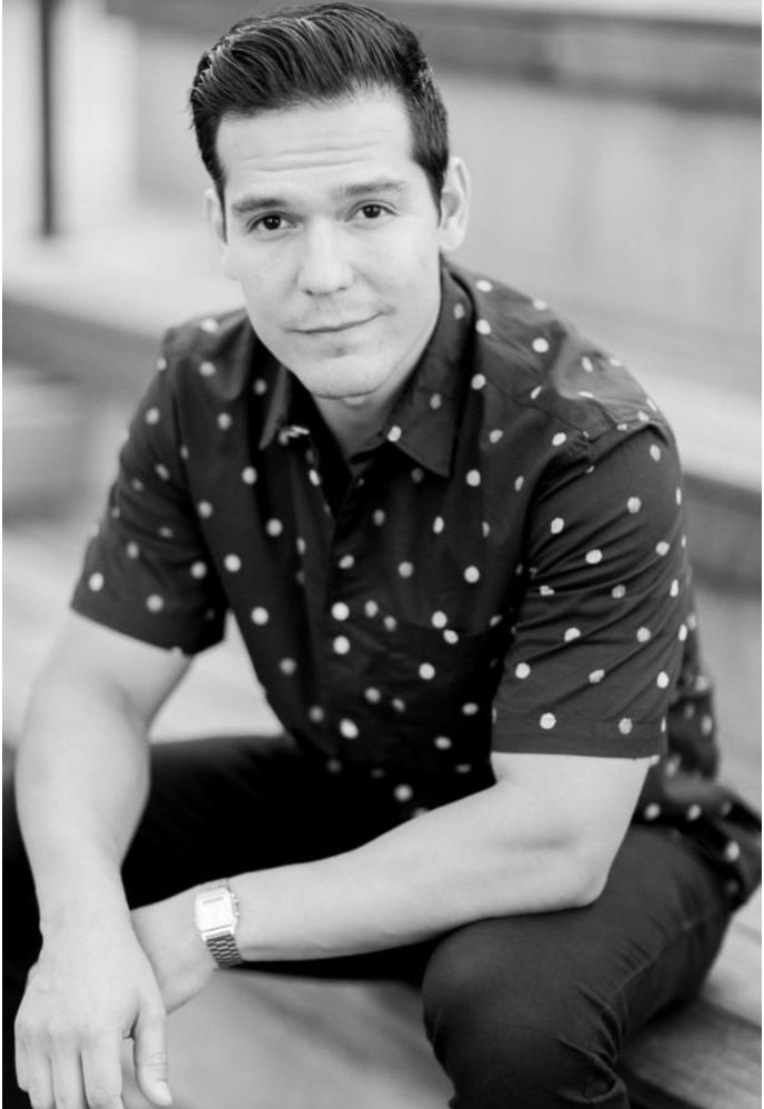 Black and white portrait of a person in a polka dot short sleeve shirt posing against a light background.