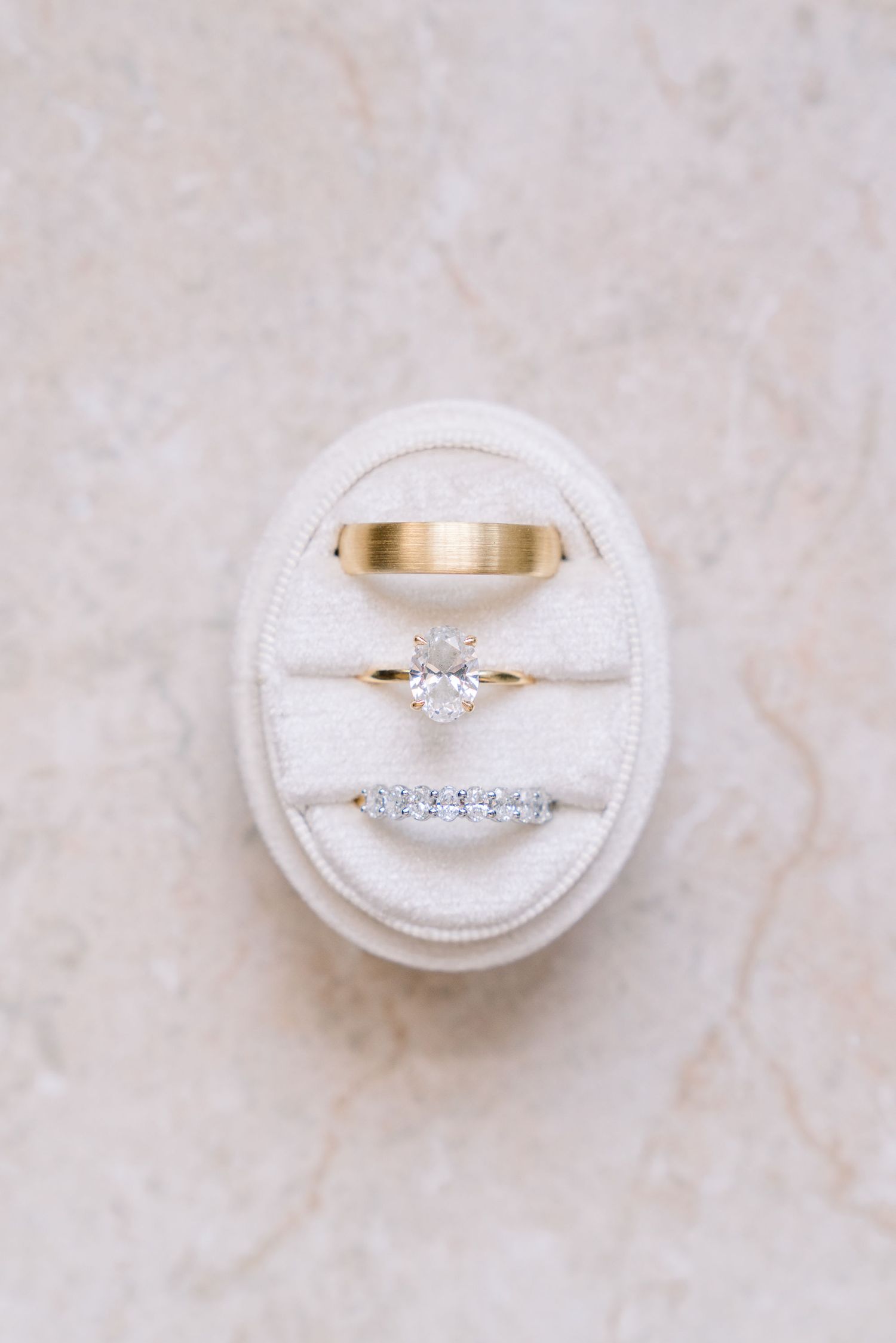 Three wedding rings including a solitaire engagement ring and diamond band displayed in a white oval ring box.