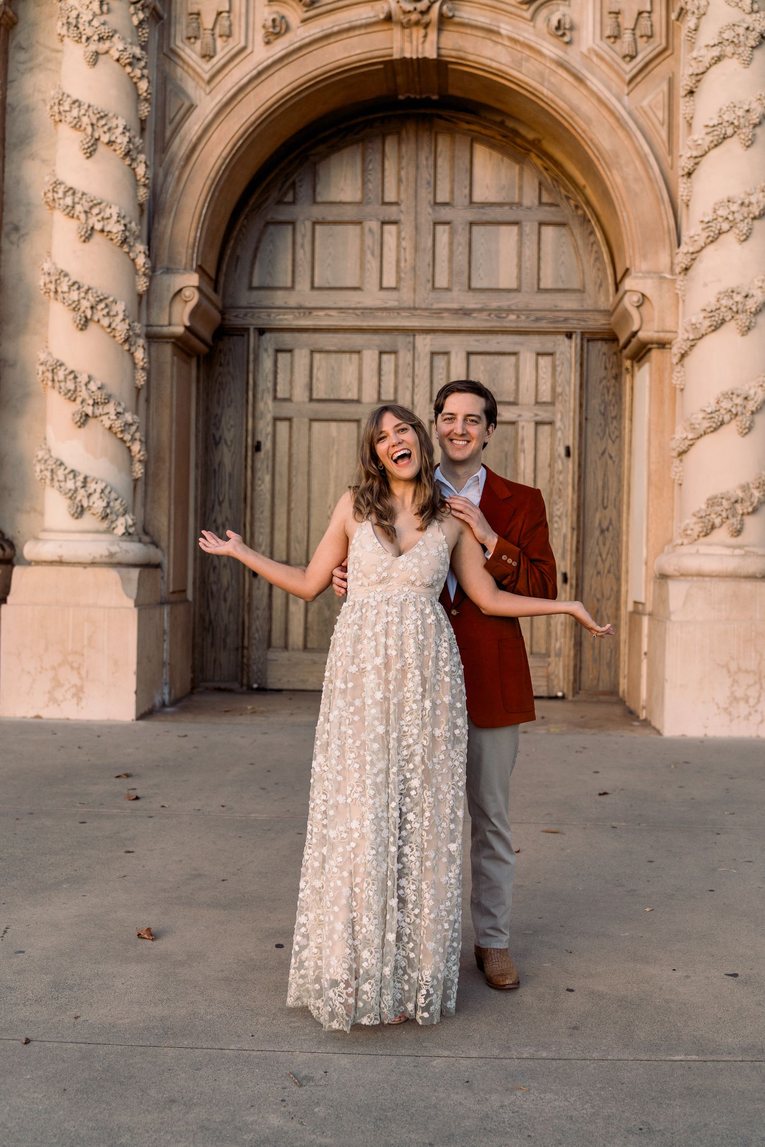 A couple poses in front of an ornate stone archway with a vintage wooden door, sharing a joyful moment together.