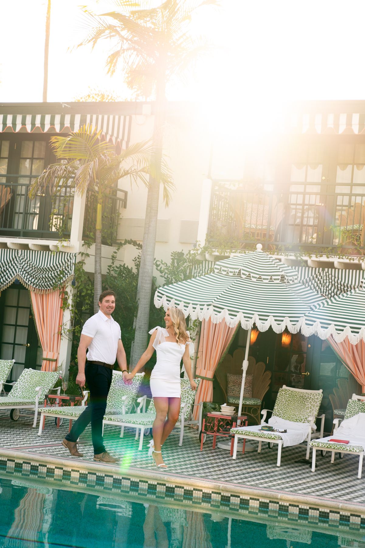 A romantic poolside scene with striped umbrellas and lounge chairs at a luxury resort during golden hour.