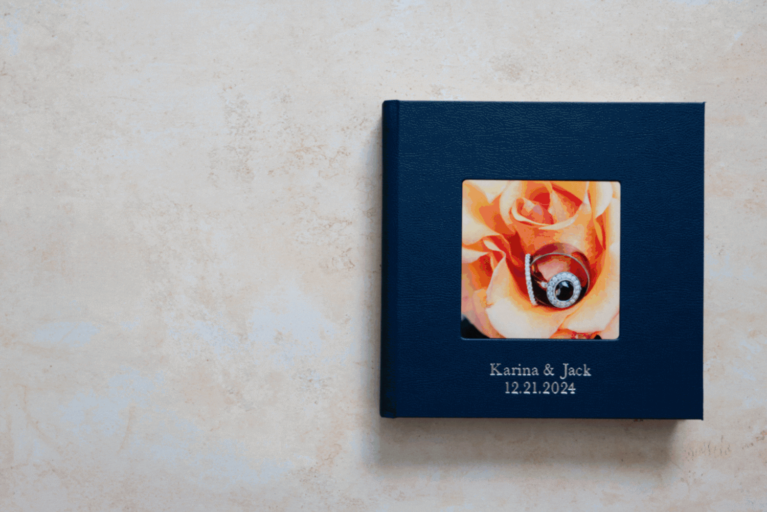 A dark blue wedding album cover with an orange watercolor design displayed on a light grey surface.
