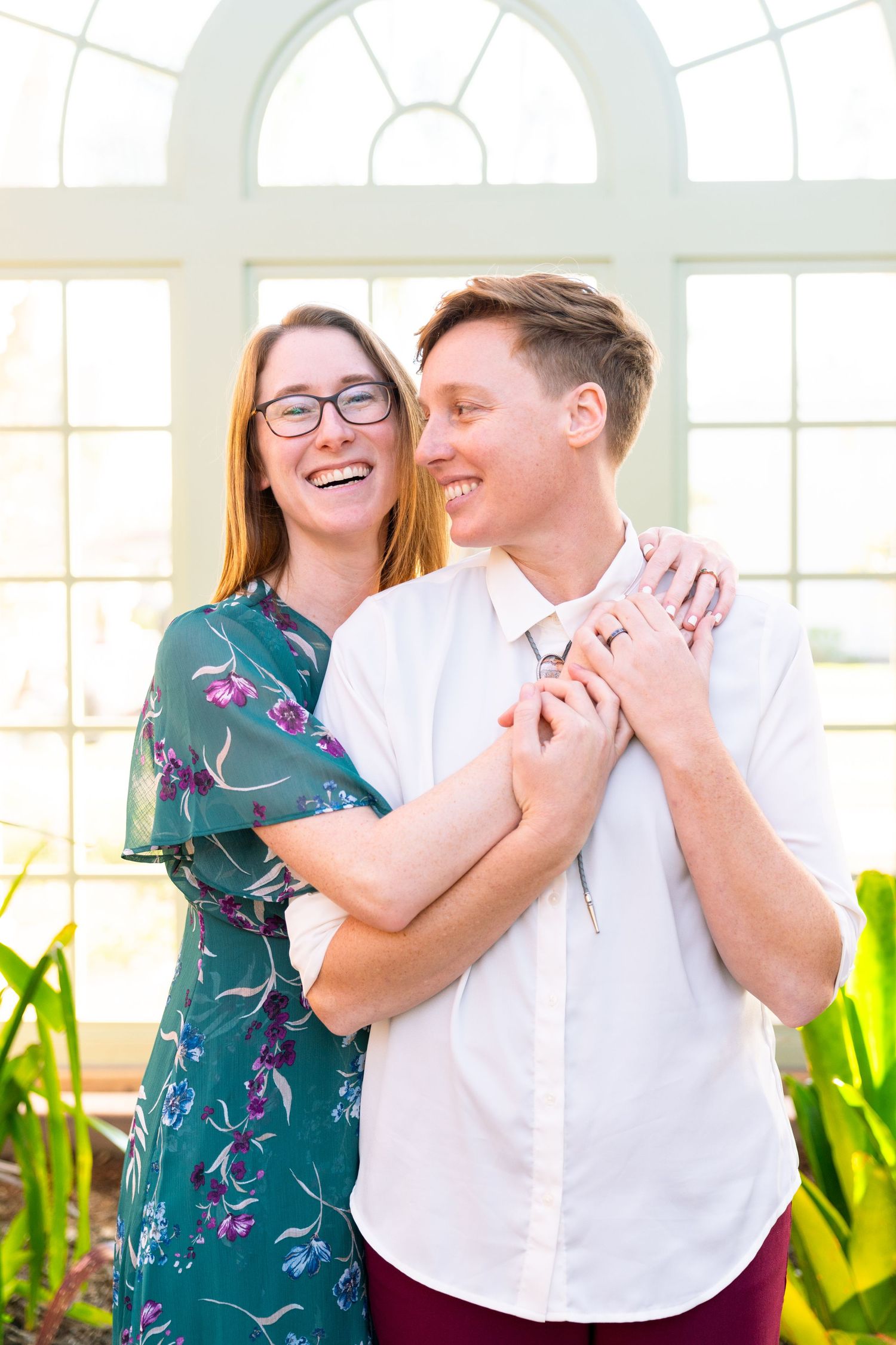 Happy couple sharing joyful laughter together in bright sunlit room with arched windows and indoor plants.