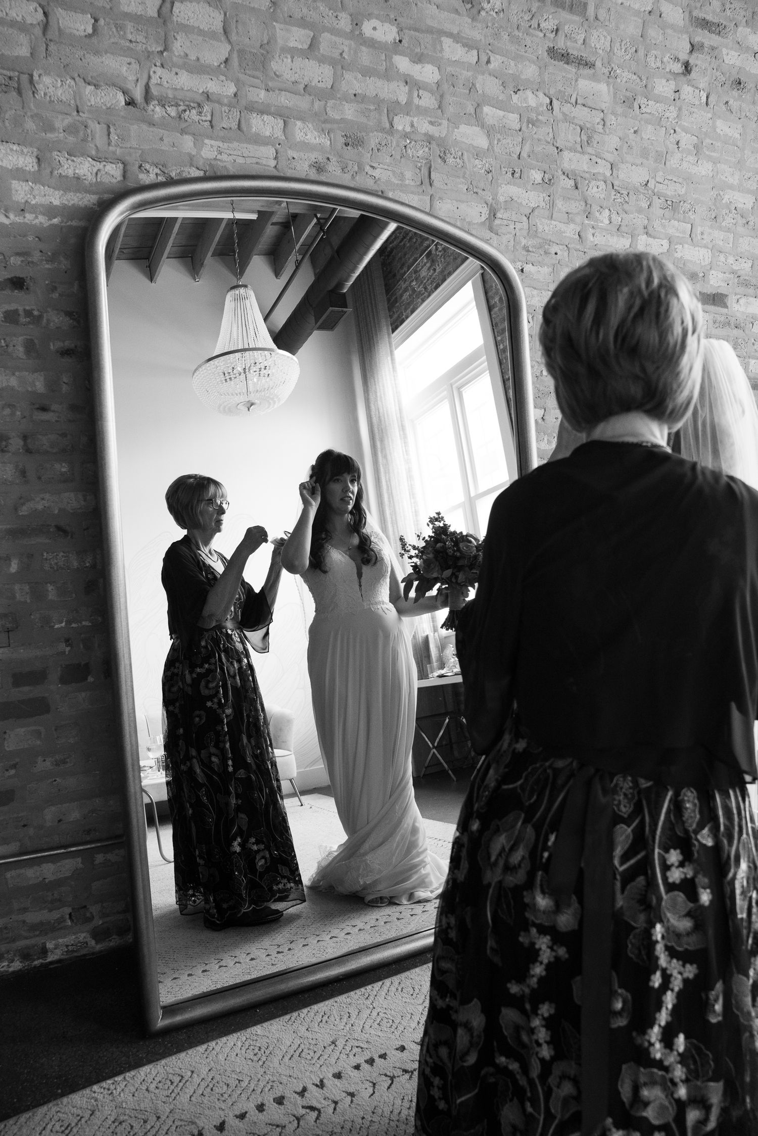 Black and white photo series showing preparations before a wedding with dress and mirror reflections in a brick-walled room.