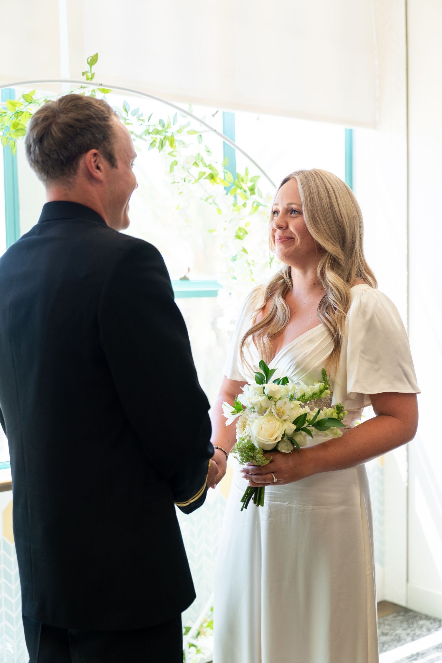 A bride and groom share an intimate first look moment at their wedding in front of white curtains with natural light.