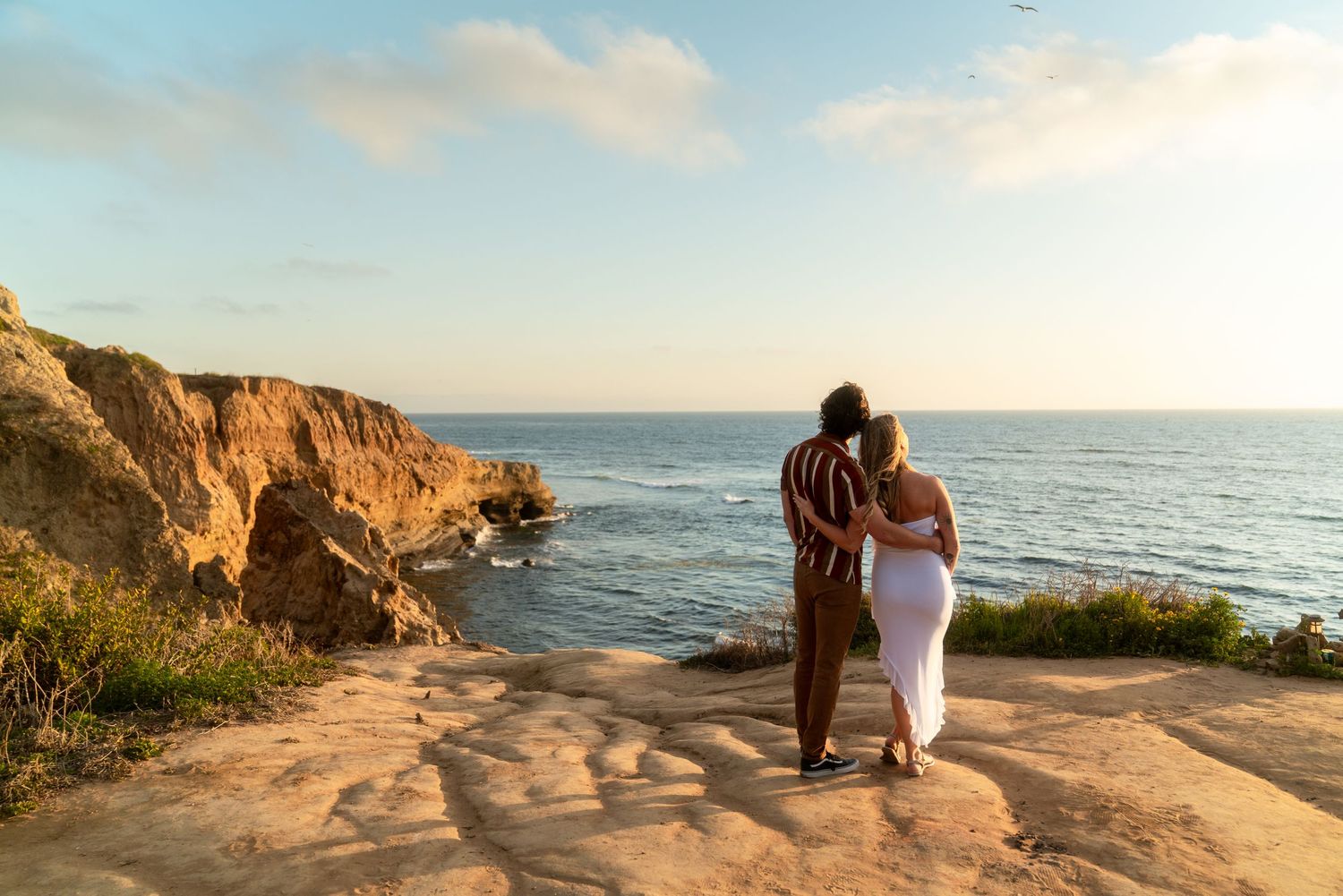 Couple enjoying sunset view from coastal cliffs overlooking the Pacific Ocean at golden hour.
