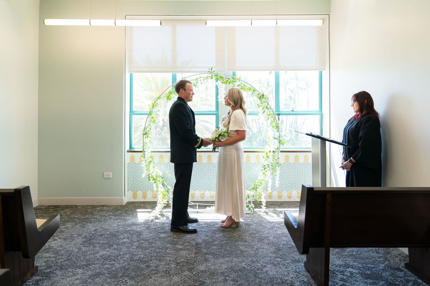 Two people in formal attire having a conversation near bright windows in an office setting.