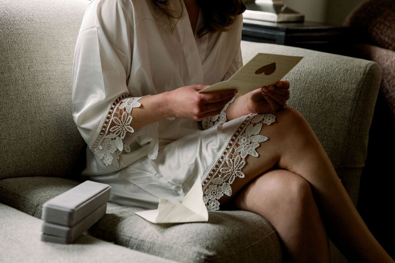 A white lace robe-clad person sits on a gray couch reading a book, with a stack of books beside them.