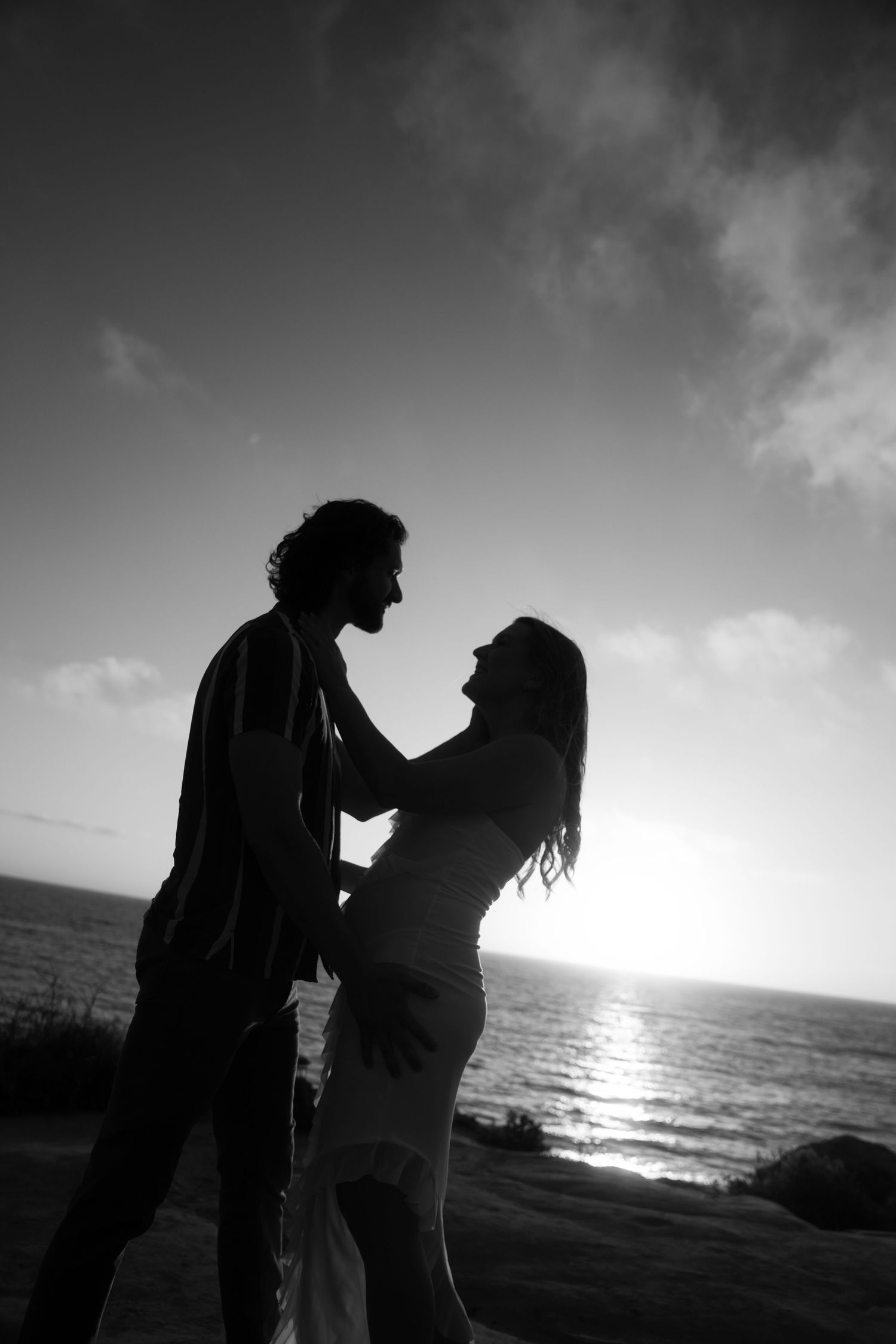 Silhouettes of a romantic couple embrace against a dramatic sunset over the ocean.