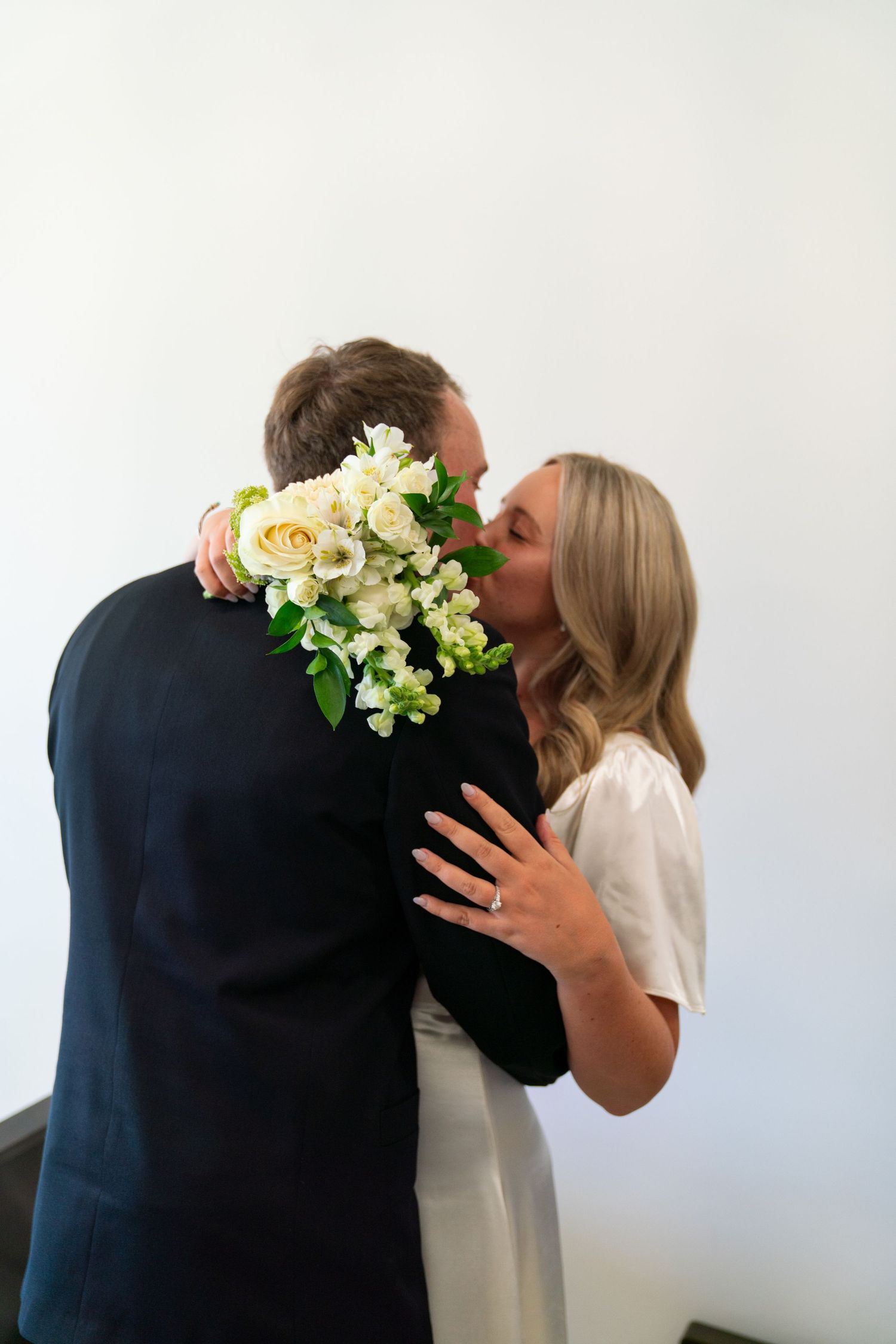 A series of three wedding photos showing a romantic embrace with floral bouquets against a white wall.
