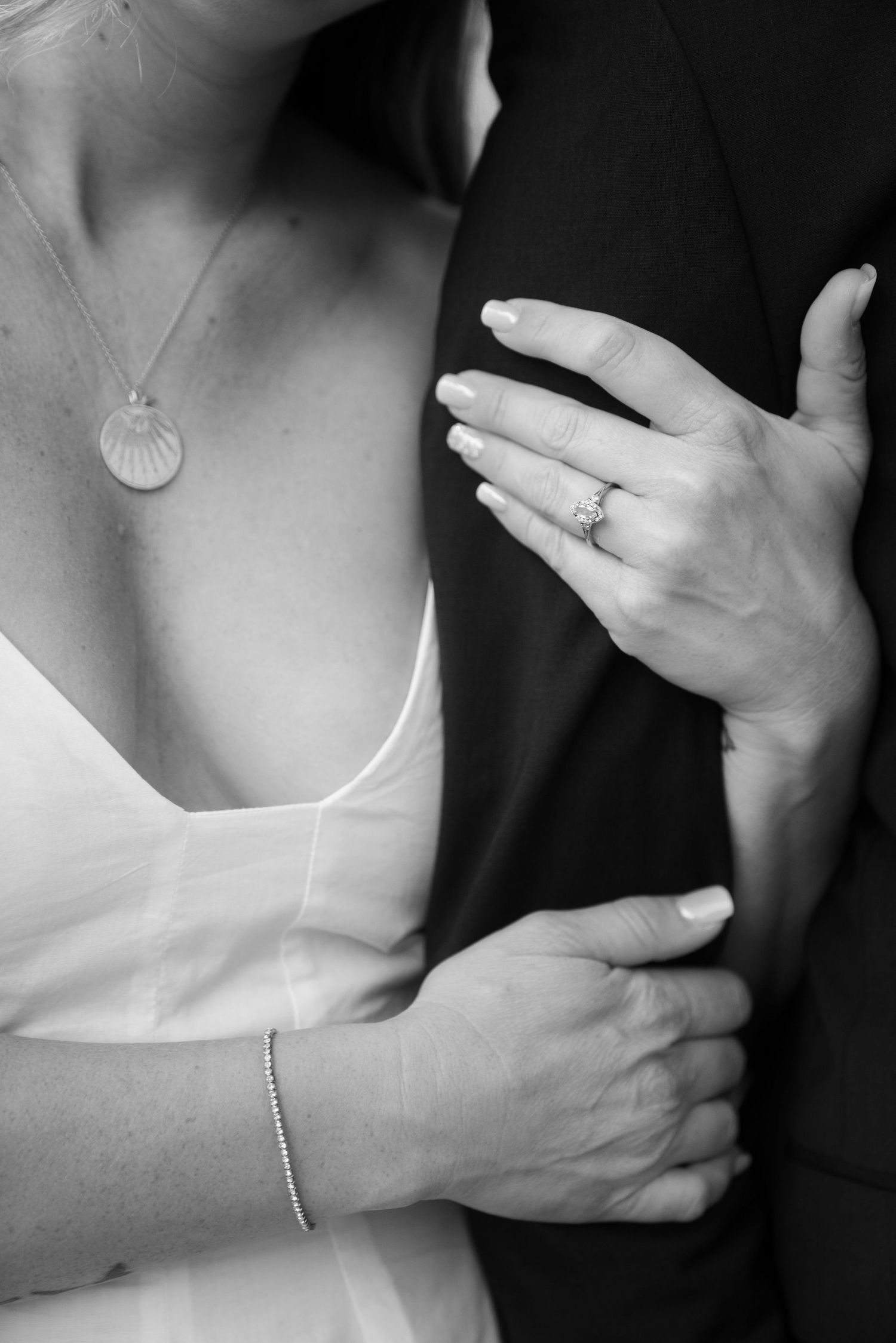 Black and white wedding photo showing a seashell necklace, white dress detail, and hands with an engagement ring.