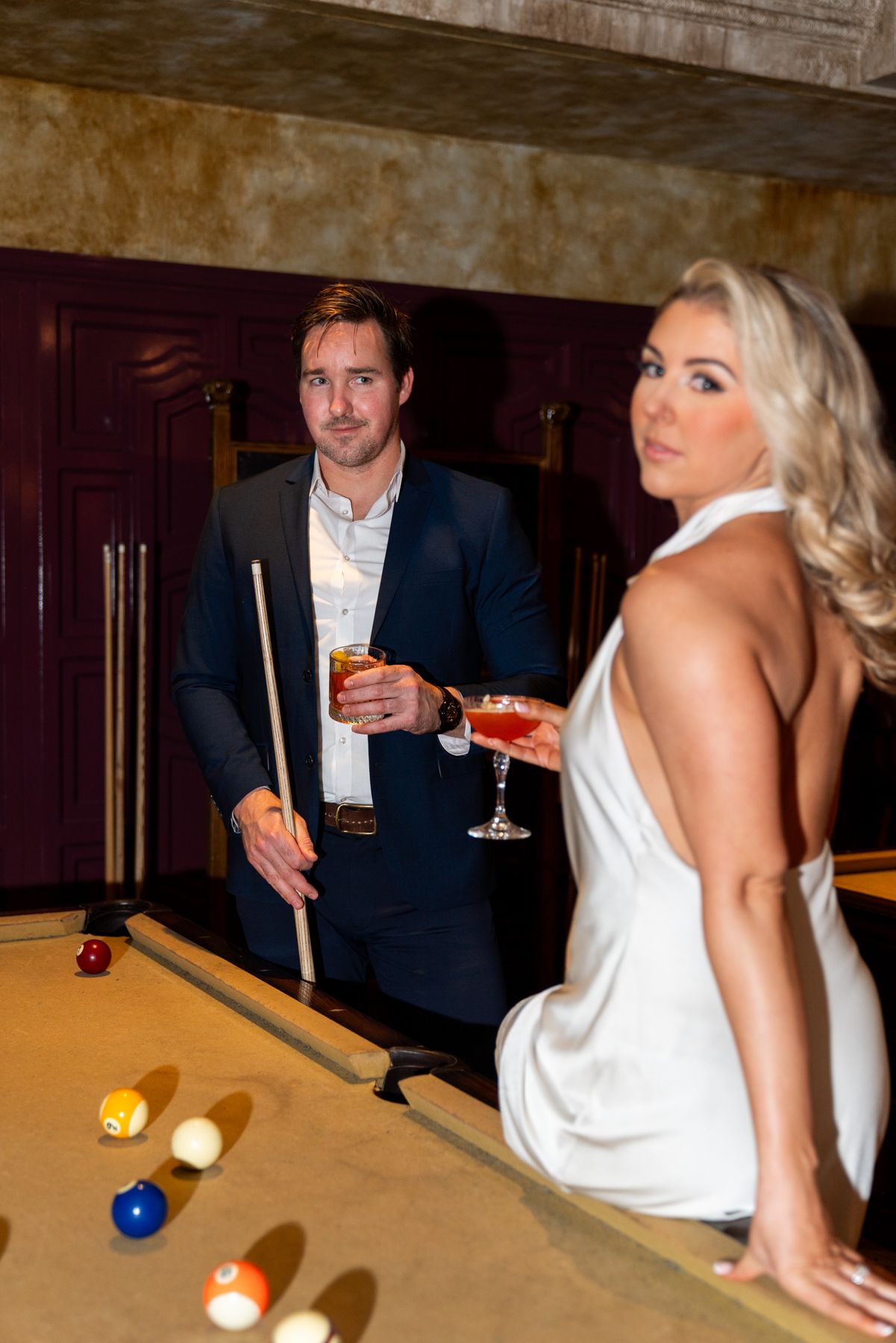 A couple enjoying cocktails while playing pool in an upscale lounge setting.
