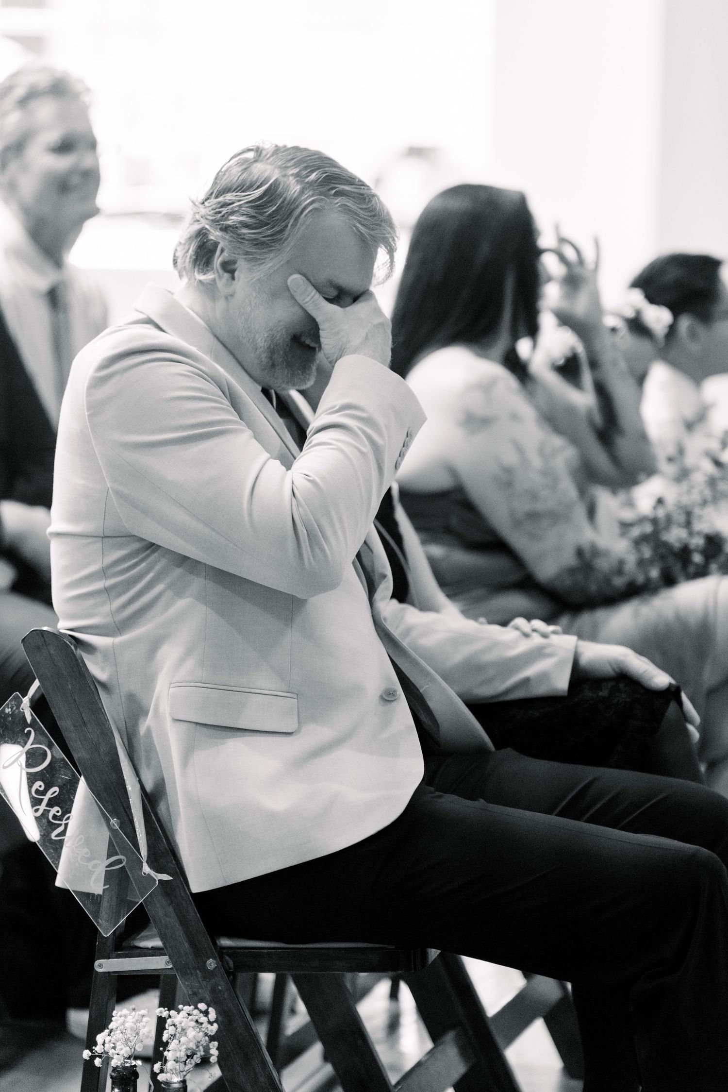 Black and white photograph of someone in a white blazer showing an emotional reaction during what appears to be an event.