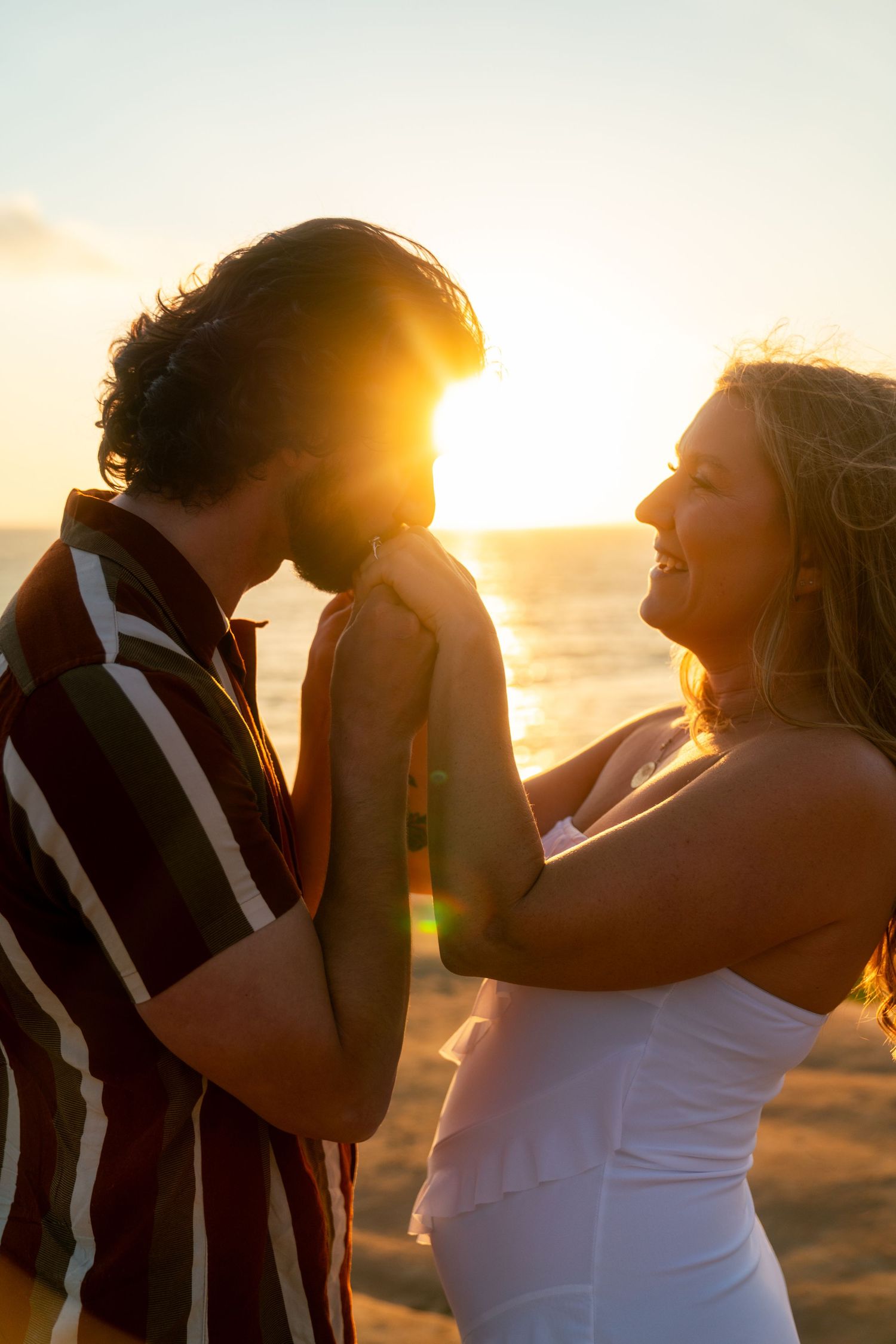 A romantic sunset moment at the beach with a couple embracing, silhouetted against the golden sun.