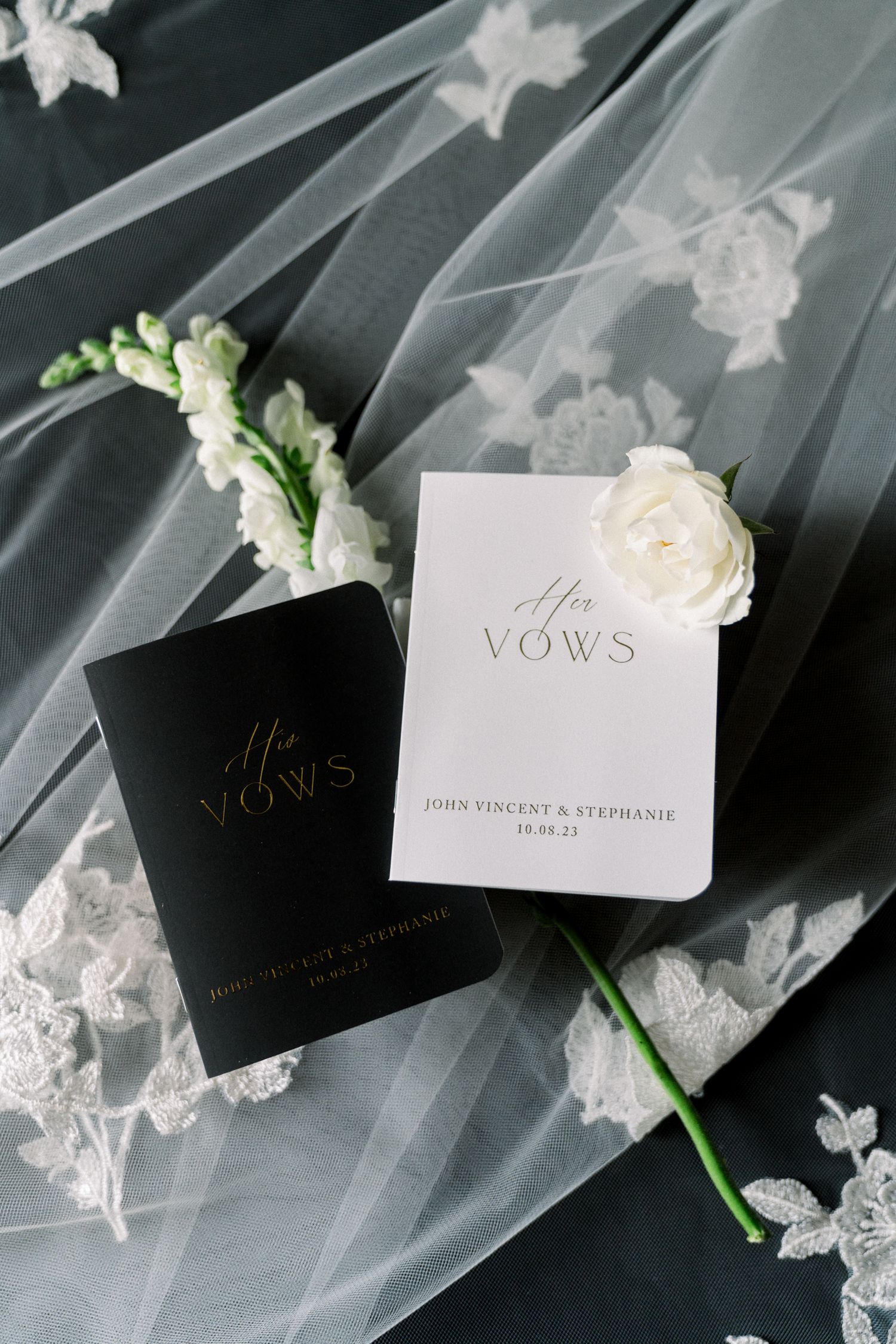 Elegant wedding vow books in black and white with roses and delicate lace veil backdrop.