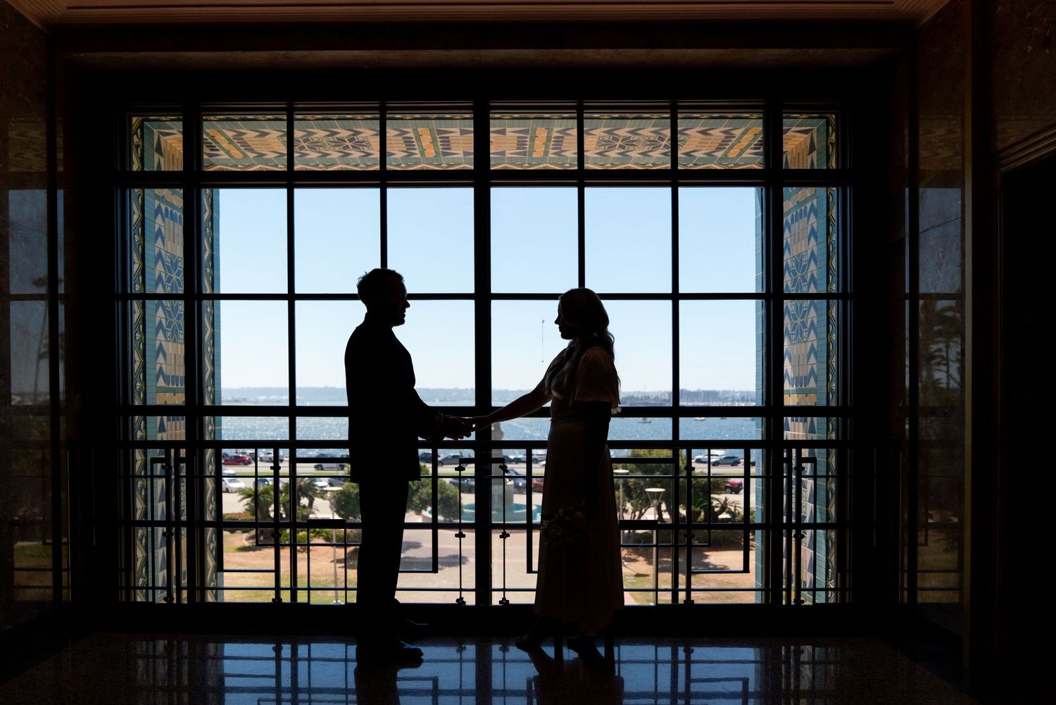 Two silhouettes stand in conversation against a large window overlooking a bright outdoor landscape.