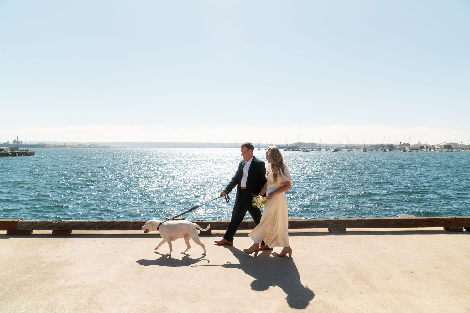 Couple sitting on wooden pier overlooking tranquil ocean during romantic coastal wedding photoshoot.