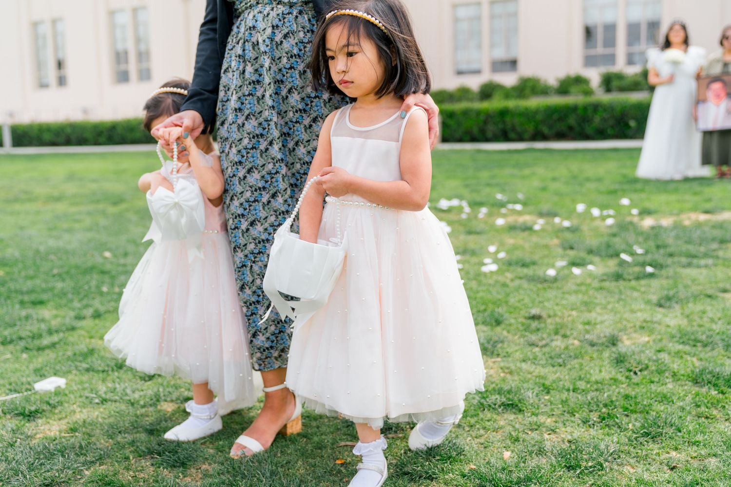 Delicate white flower girl dresses flow in the breeze as the children play together on a lush green lawn.