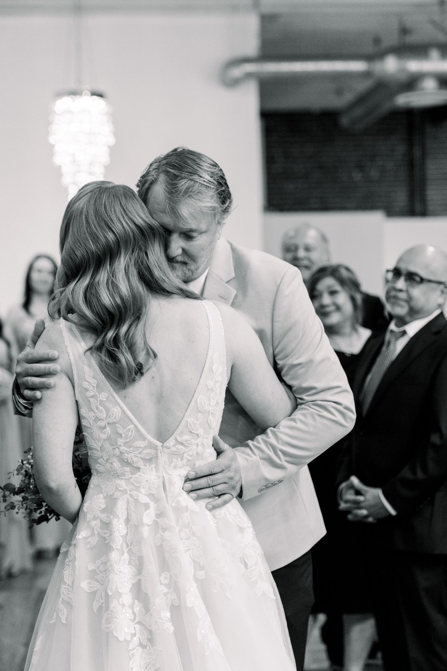 A couple shares their first dance at a wedding while guests smile and watch in the background.