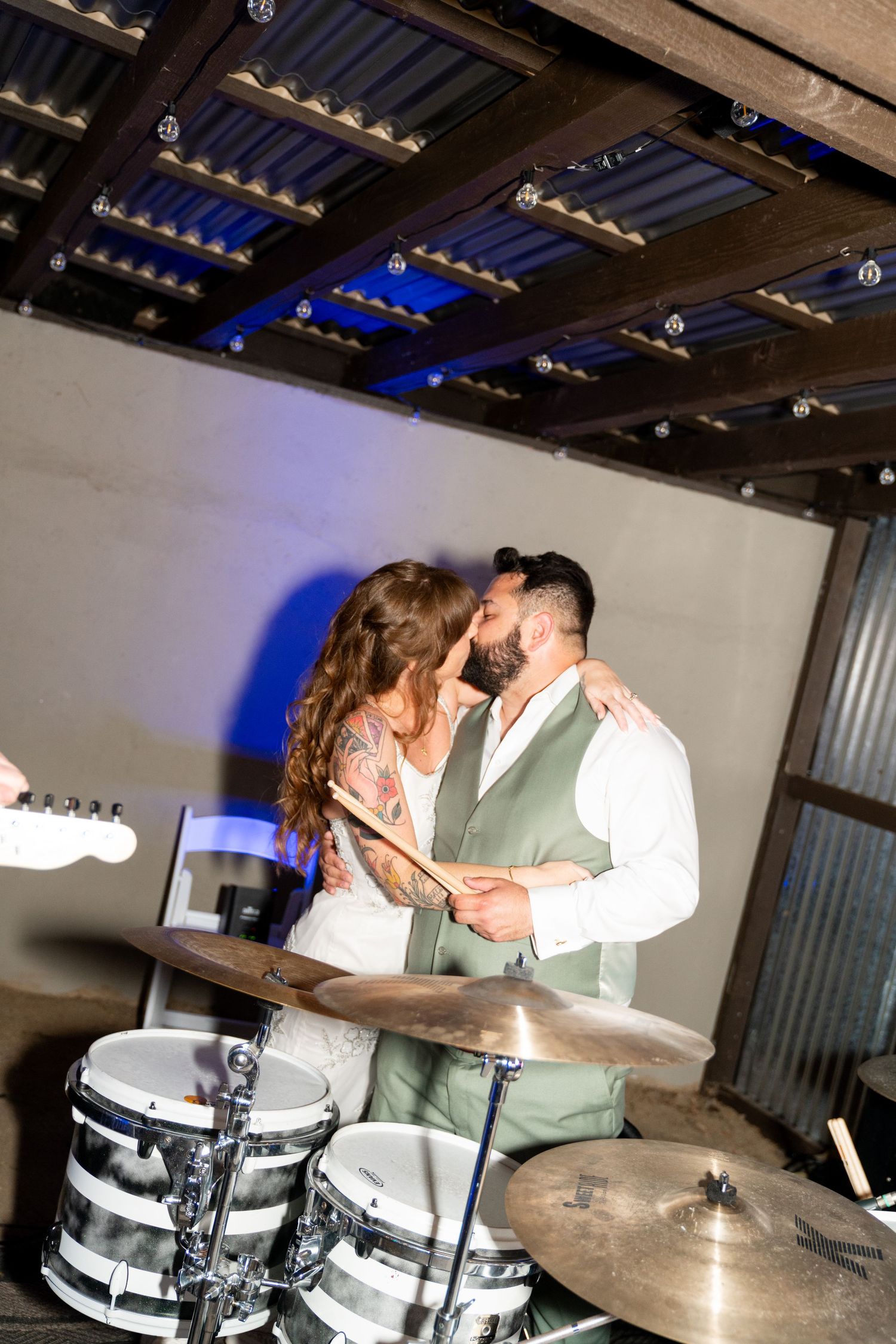 A couple in formal attire share tender moments while posing in an industrial venue with exposed ceiling and drum kit.
