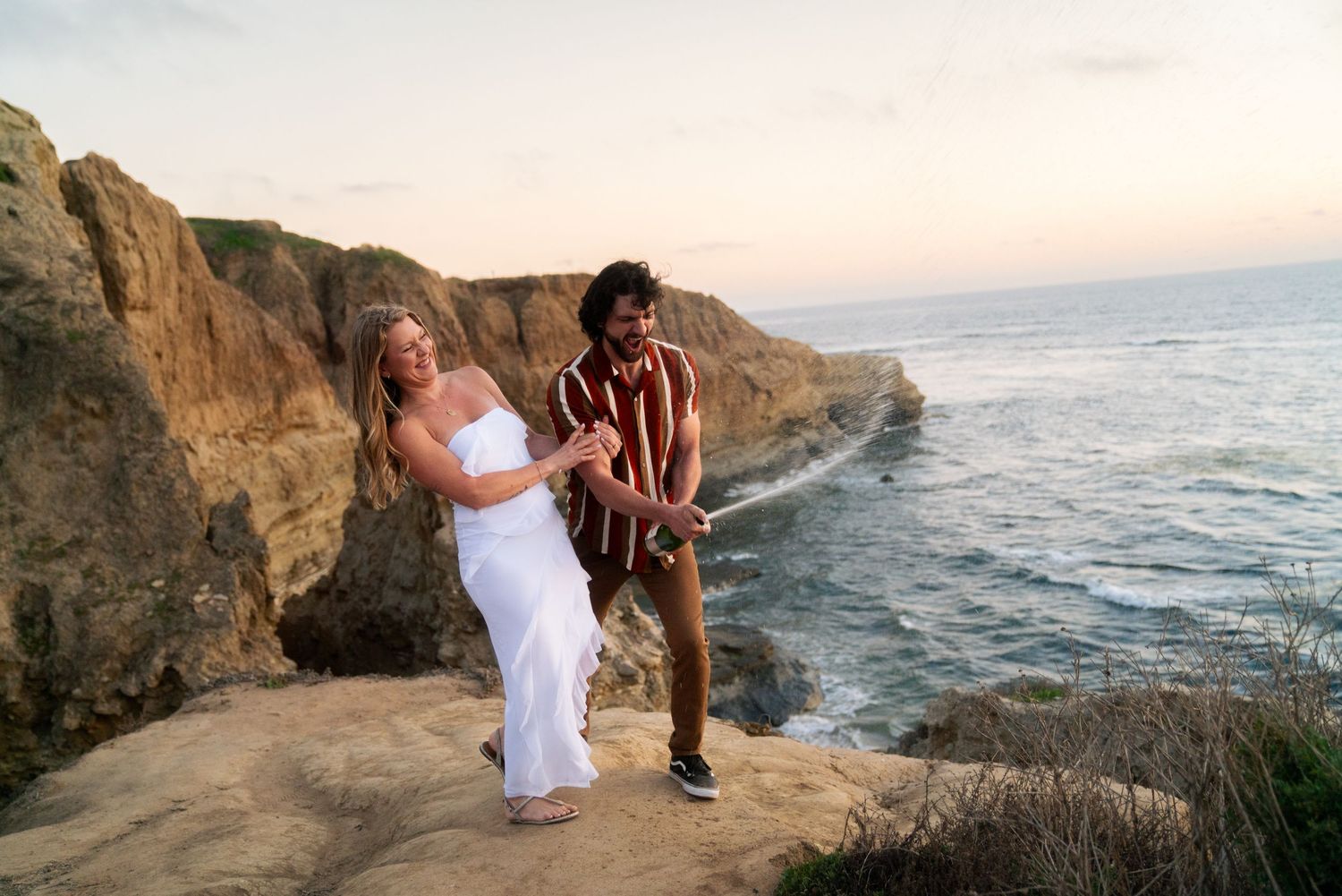 A couple enjoys a romantic moment on ocean cliffs during sunset.