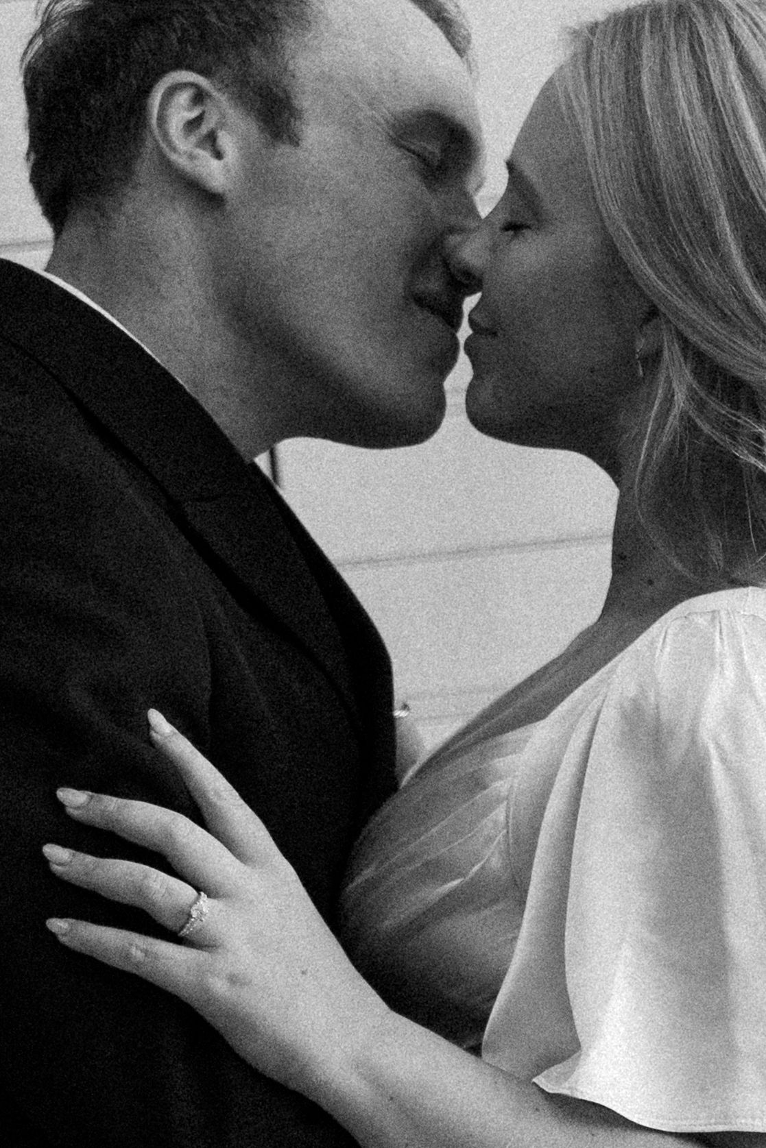 A romantic black and white photograph of a couple sharing an intimate kiss, with the woman wearing white.