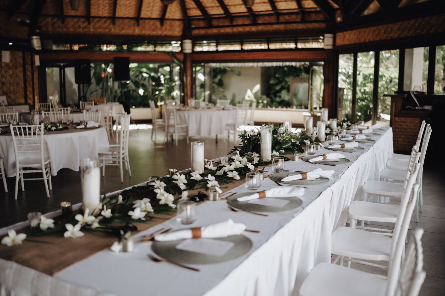 Wedding reception venue decorated with white tablecloths, wood accents, and elegant floral centerpieces in a rustic setting.
