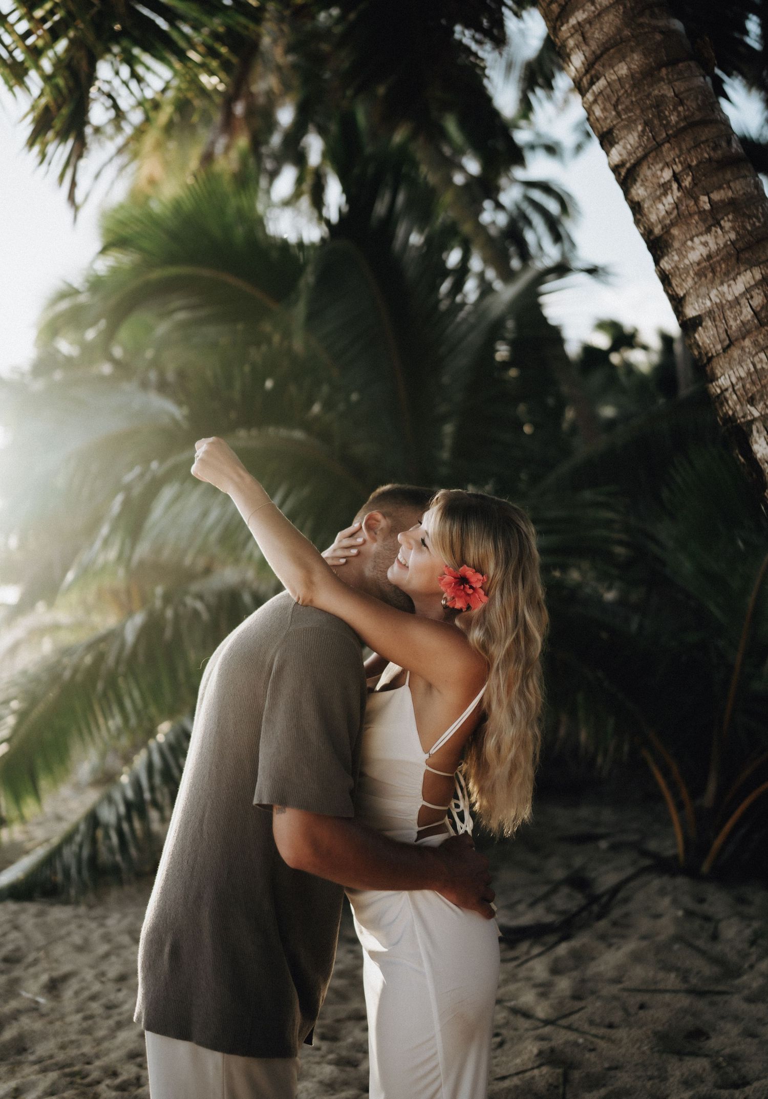 Romantic couple shares intimate moments under swaying palm trees on a tropical beach at sunset.
