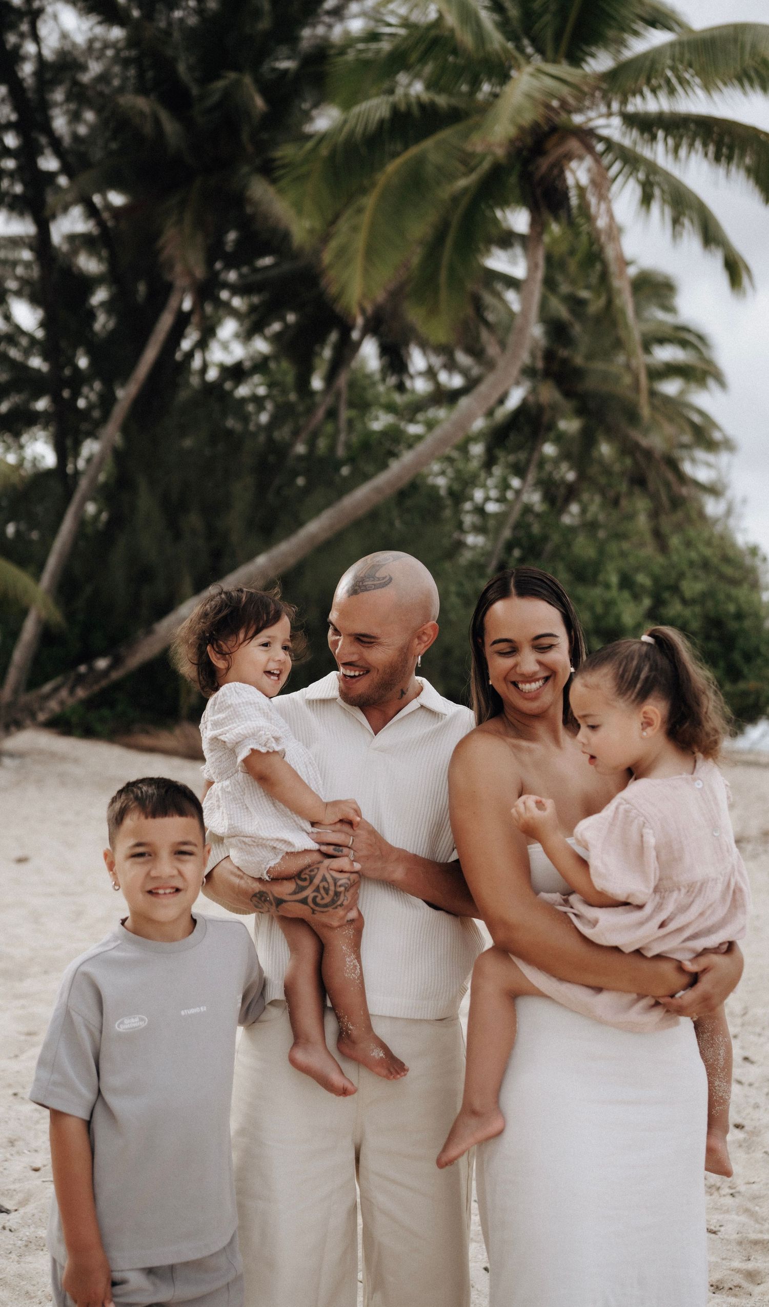 A family shares joyful moments together on a tropical beach with palm trees in the background.