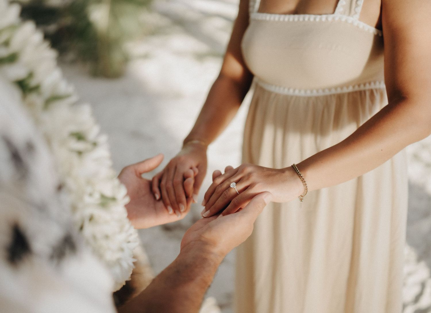 Hands exchanging rings during an intimate wedding ceremony with white floral decorations in the background.