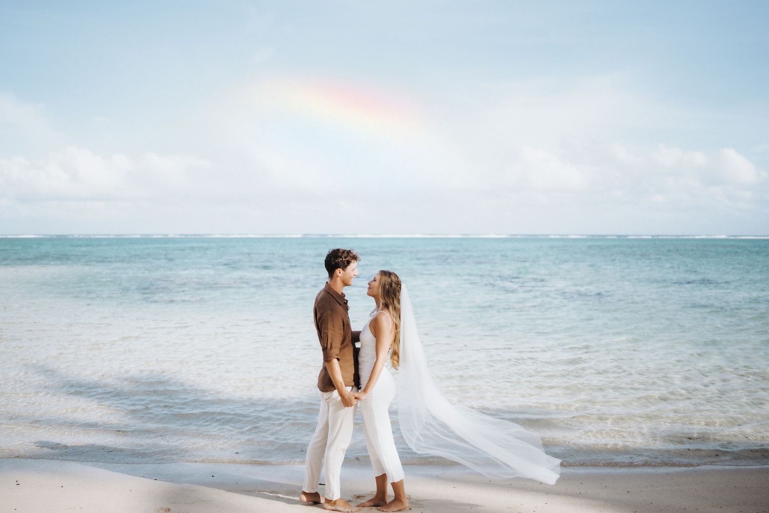 A romantic beach wedding photoshoot with couple embracing by the ocean as waves roll in during sunset.