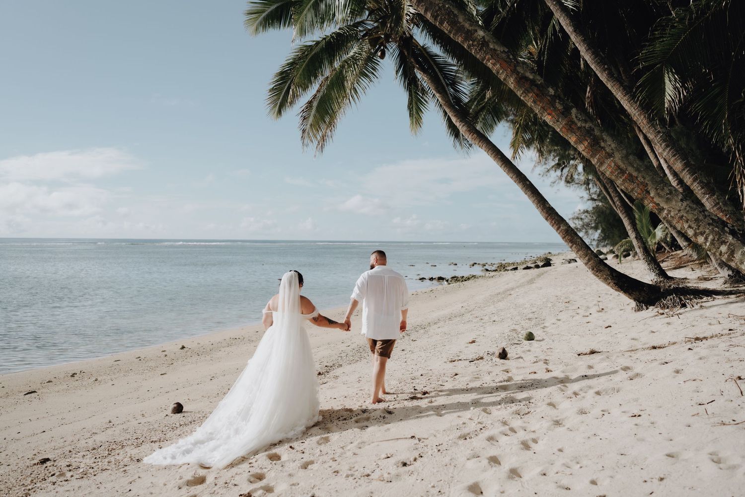 Two people holding hands walk on a white sandy beach with leaning palm trees and ocean views in a tropical destination.