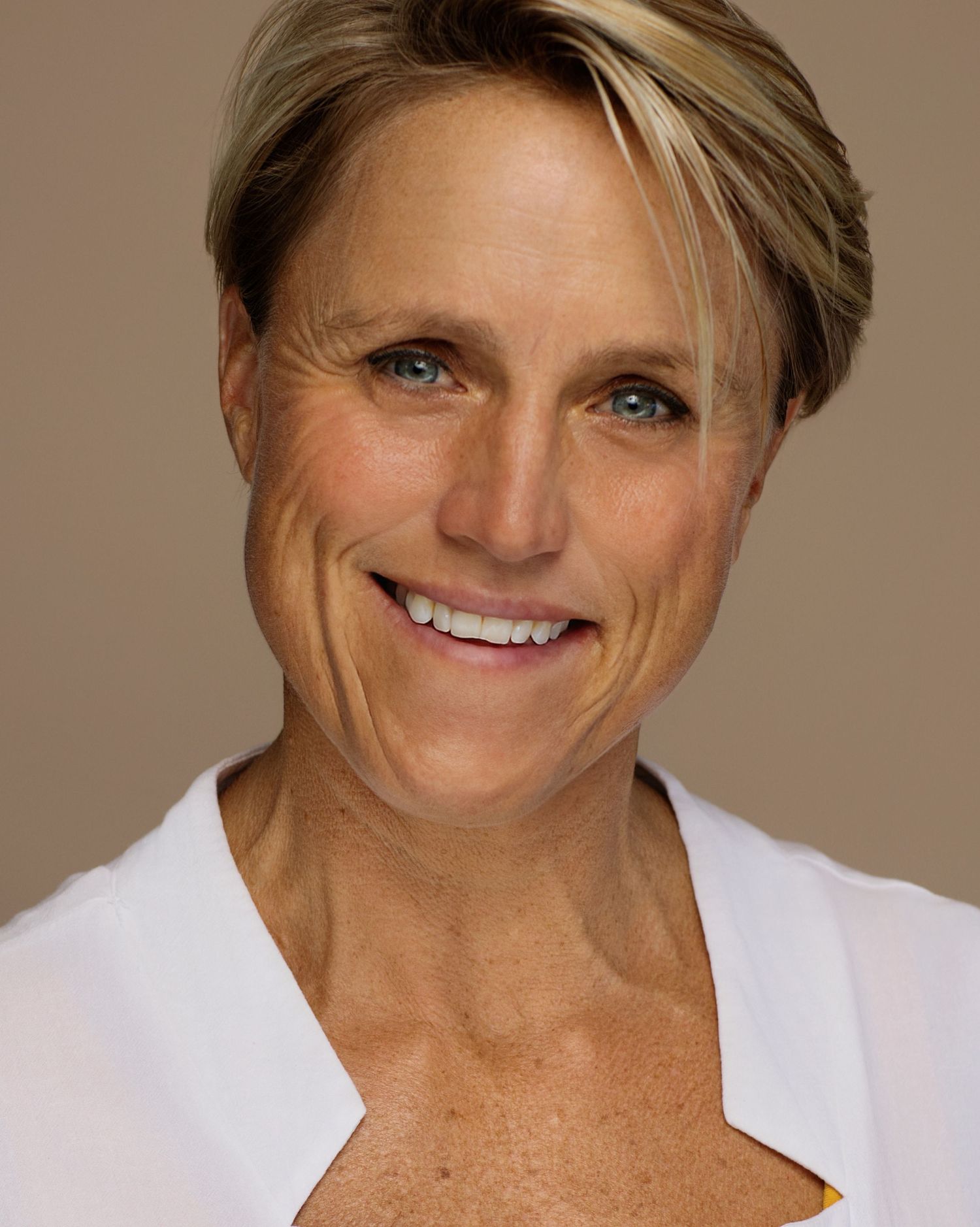 Smiling athletic person wearing a white top against a neutral beige background.
