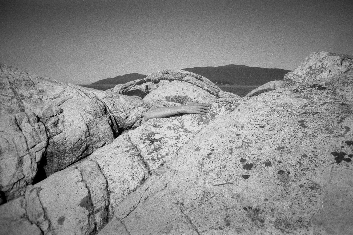 Black and white photo of rugged rocky landscape with natural stone arch formation and distant mountains.