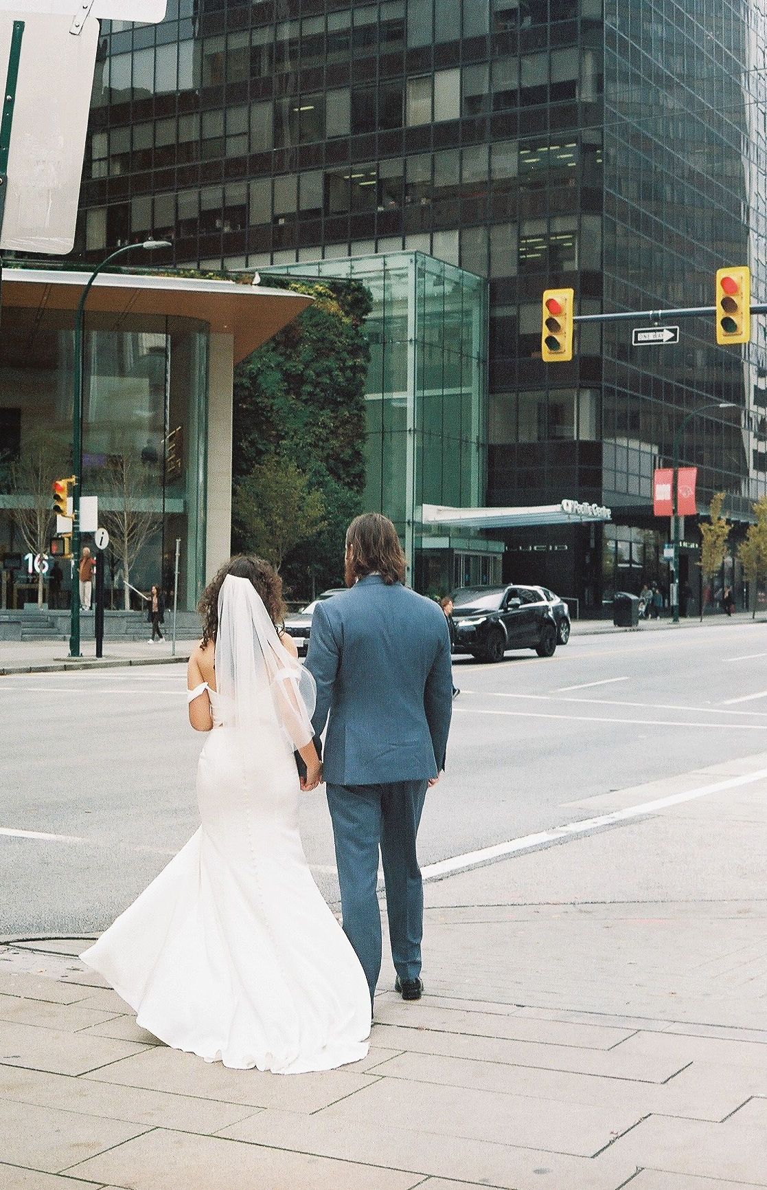A bride and groom walking down a modern city street with glass buildings in the background.