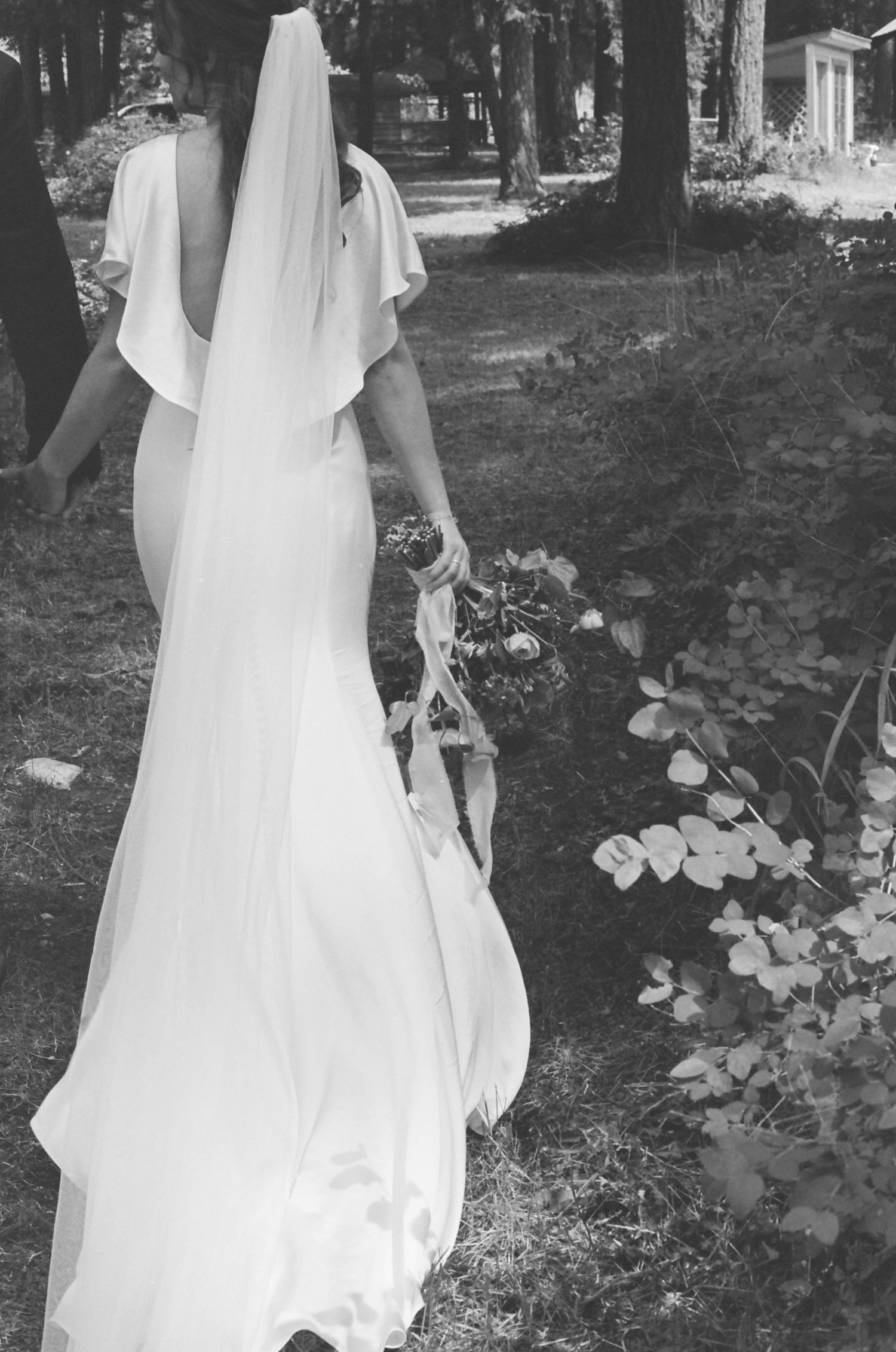 Black and white portrait of flowing wedding dress details in a wooded garden.