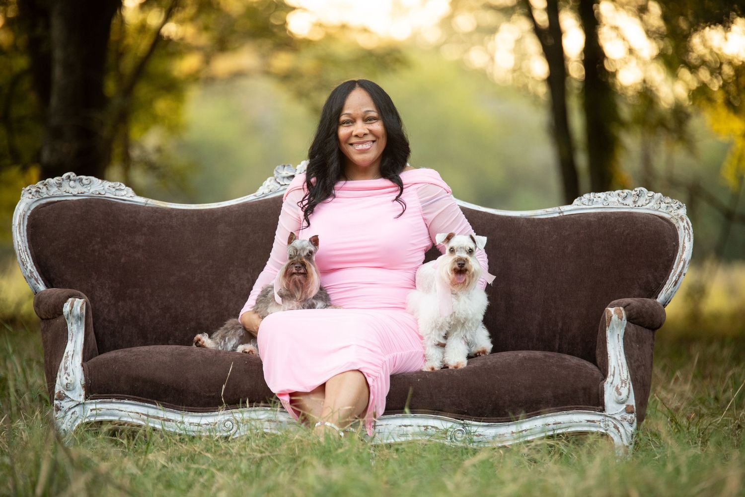 woman wearing pink dress sitting on antique couch with her two miniature schnauzer dogs. 50th birthday portraits.