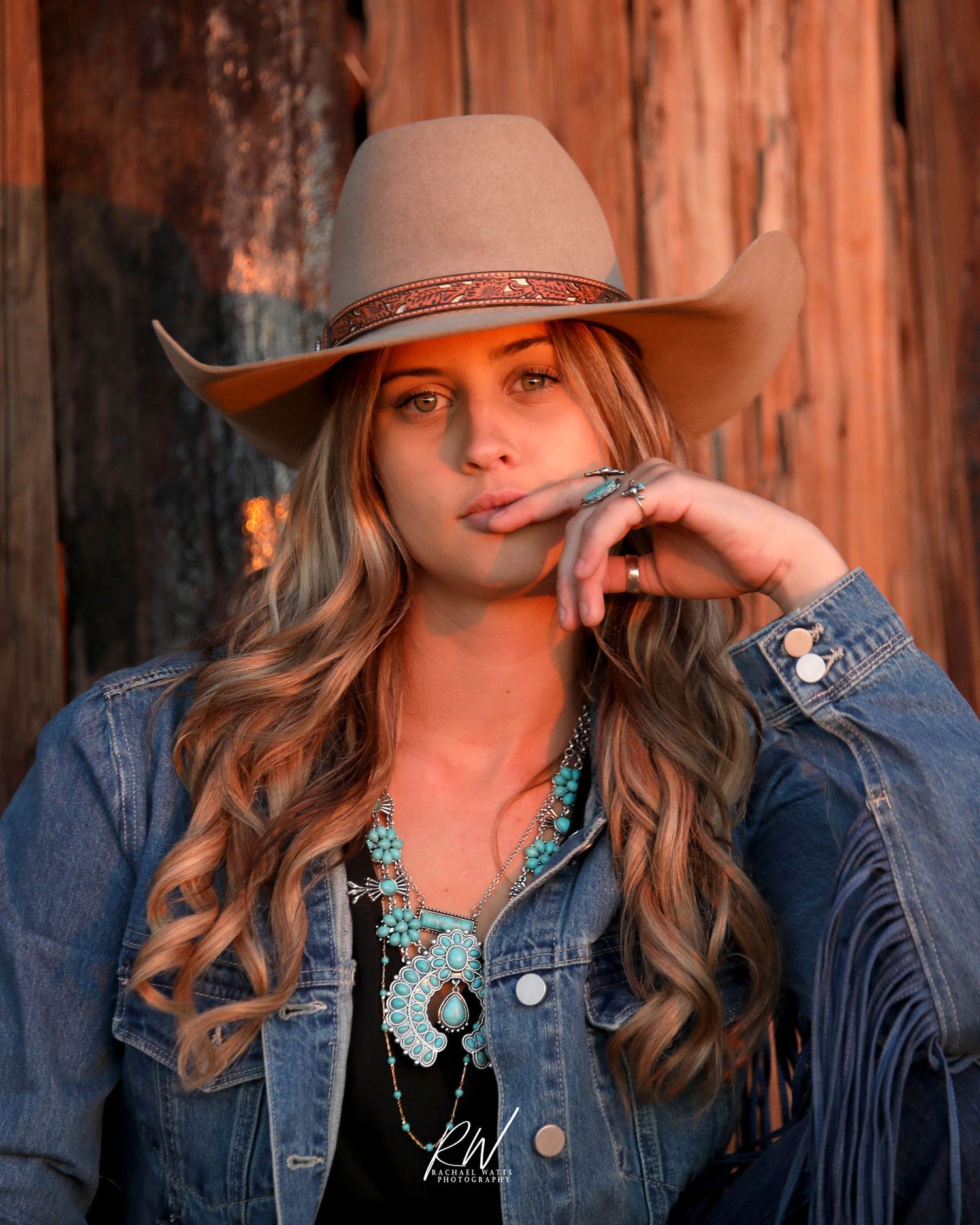 western branding photographer. cowgirl sitting next to wood wall wearing denim and turquoise.