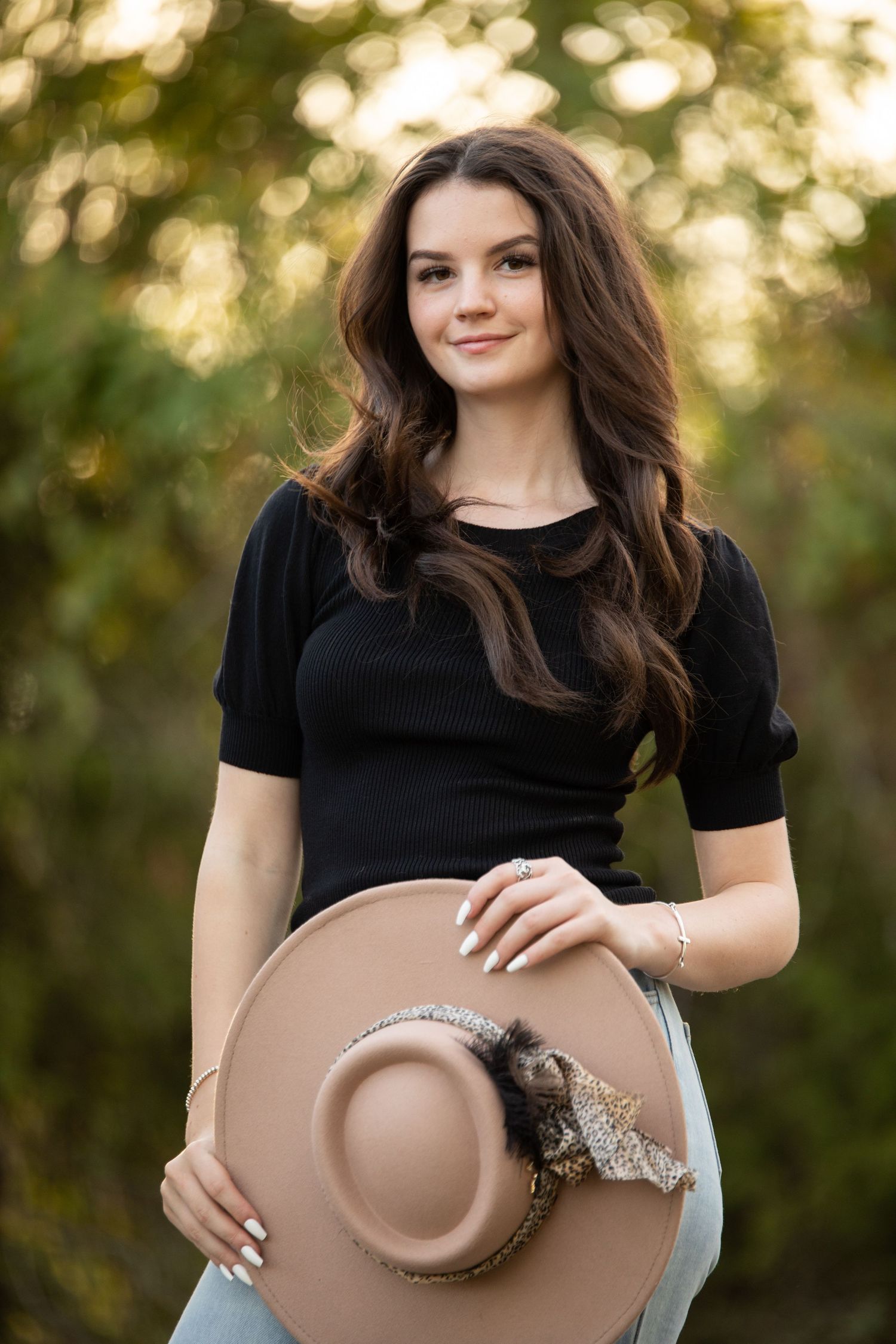 senior photo shoot, girl standing in front of trees holding a hat.