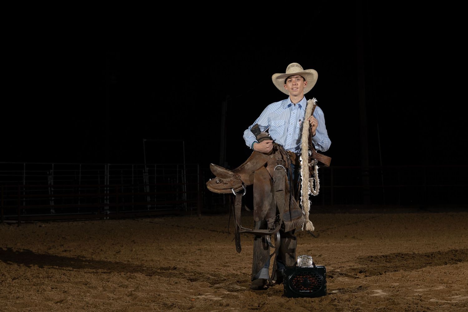 youth rodeo contestant holding his saddle and bronc halter. Western senior portraits.