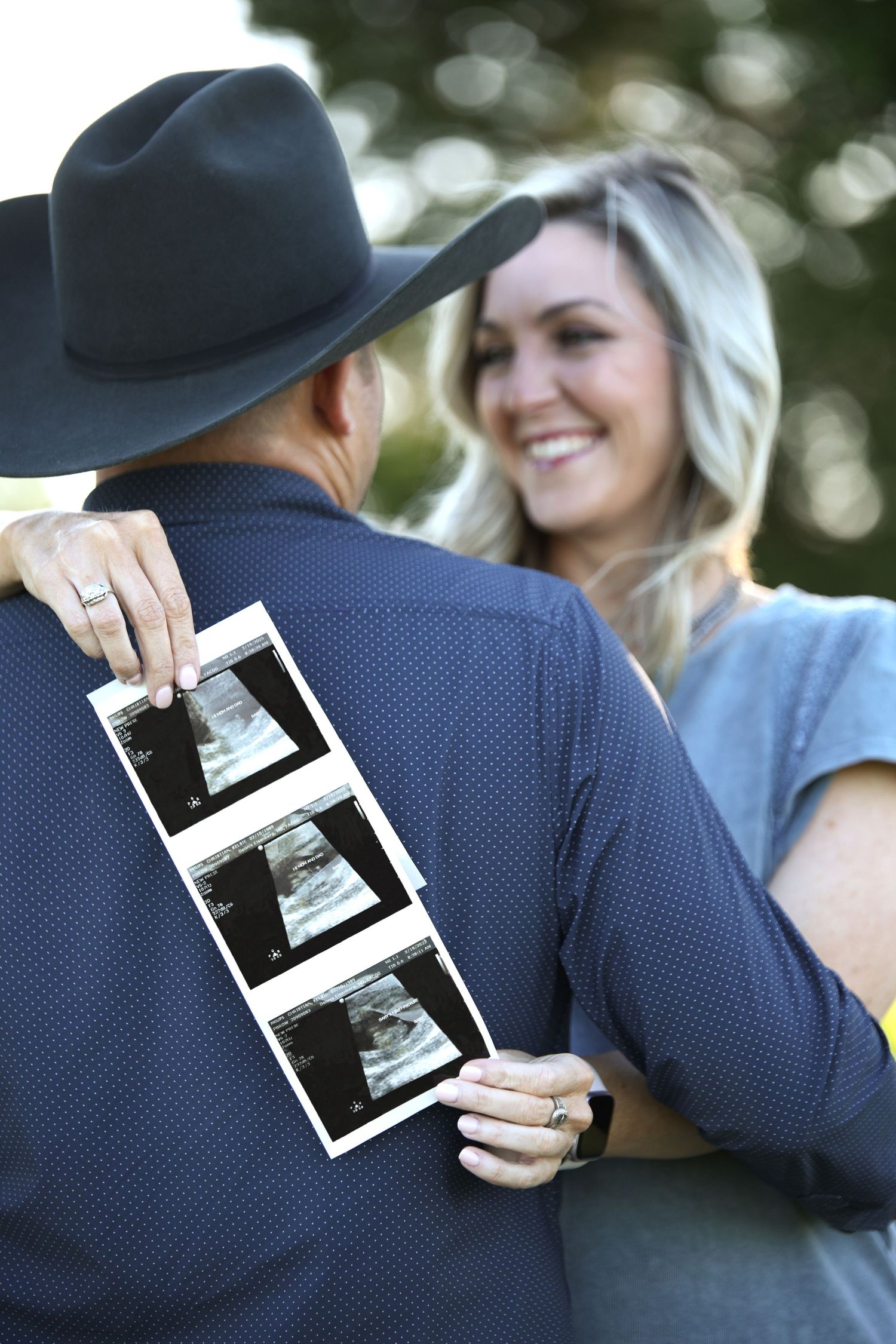woman holding sonogram images around partners back smiling. Baby announcement.