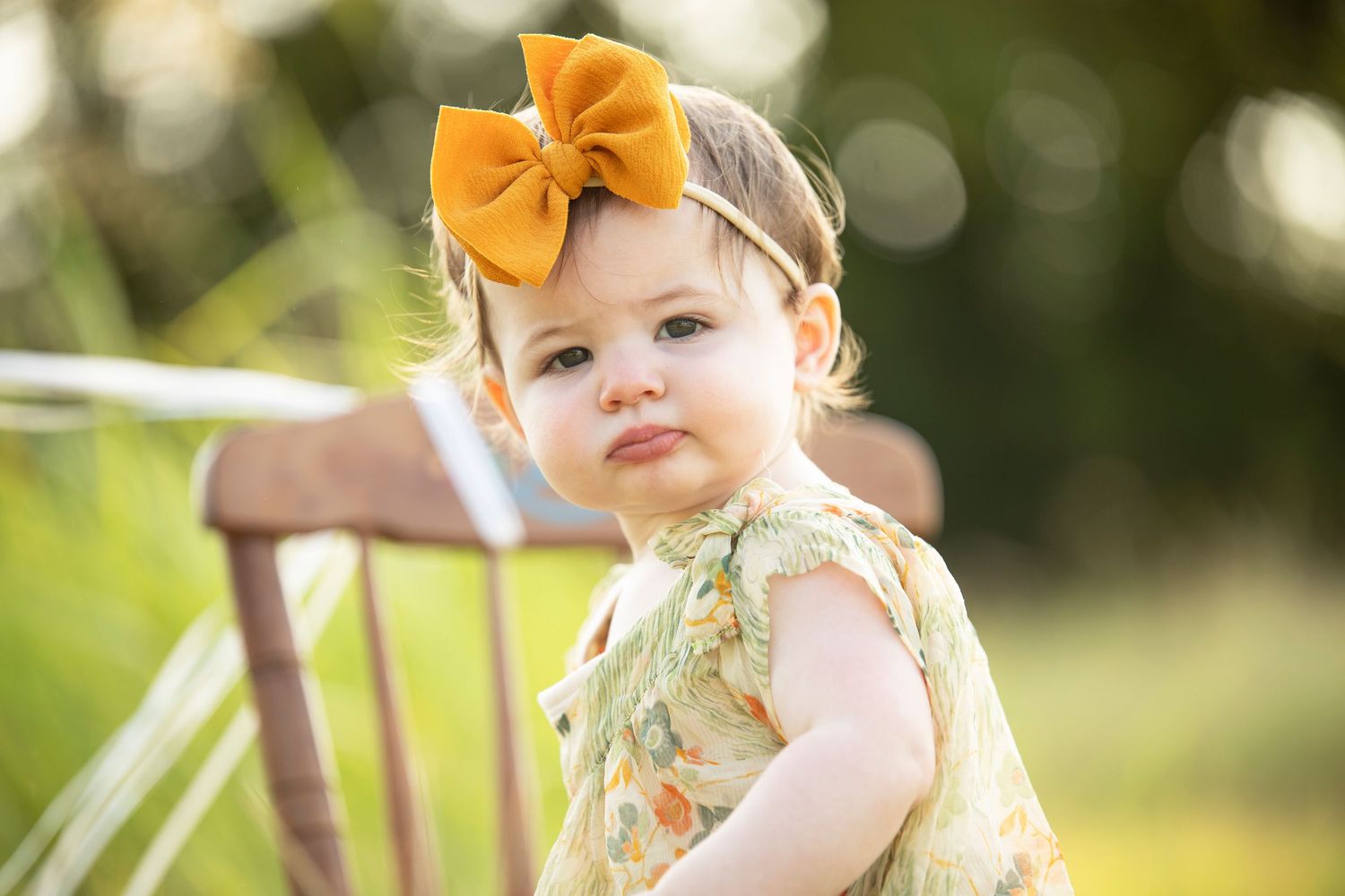 Caddo Mills portrait photographer. Baby girl with orange bow looking over her shoulder with a curious expression.