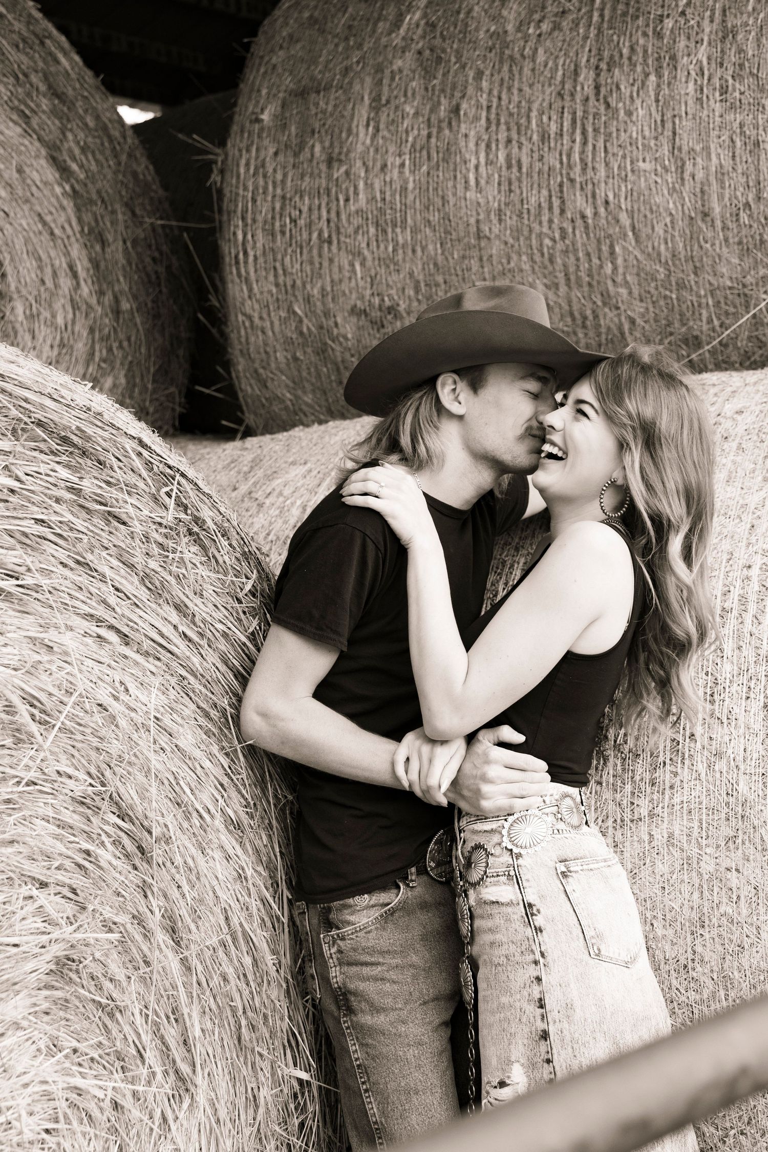 A couple laughing in front of a haybale during their engagement session at their family's farmland in Northwest Iowa.
